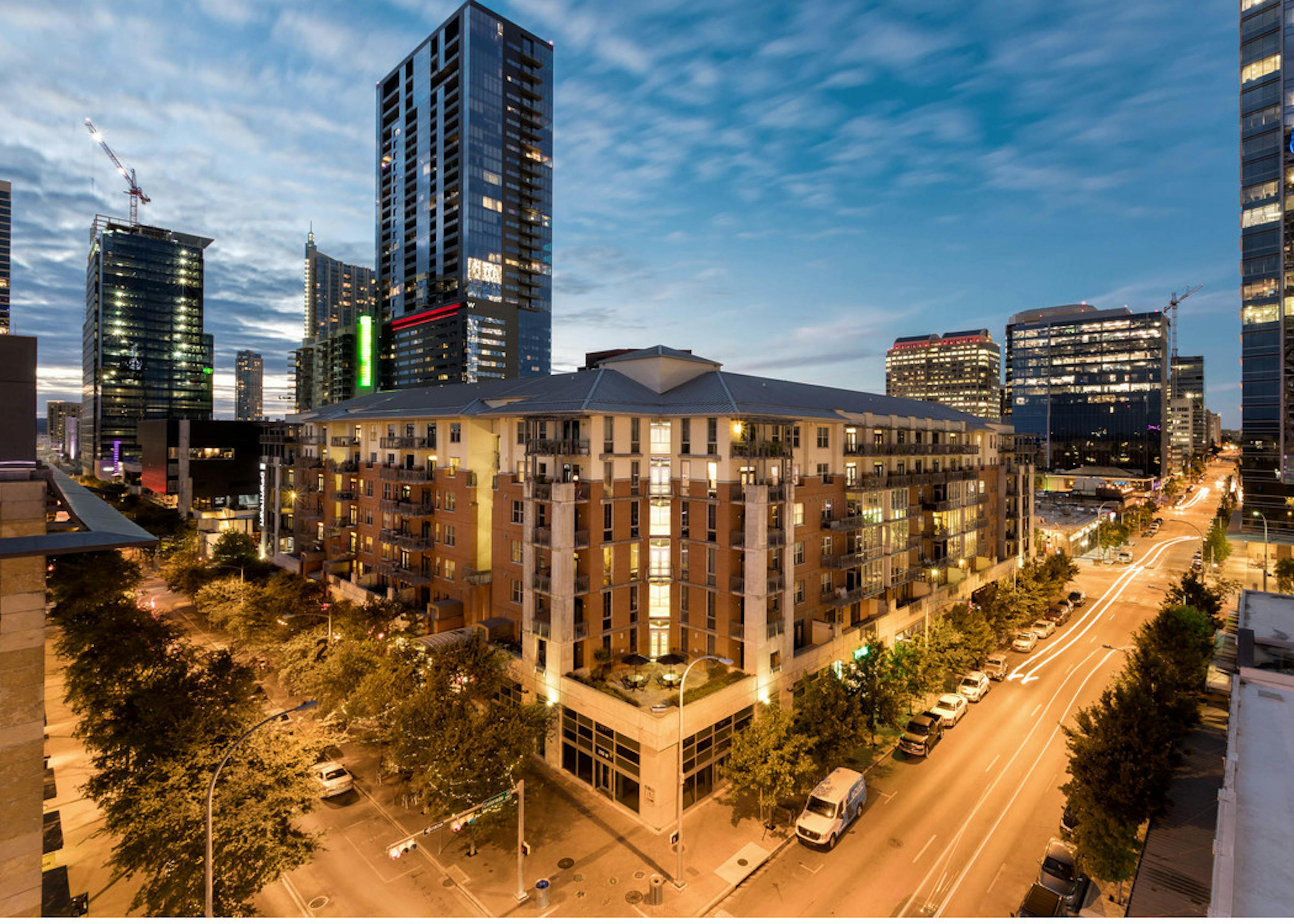Exterior view of AMLI Downtown apartment community building at nighttime with nearby trees, lamp posts and buildings