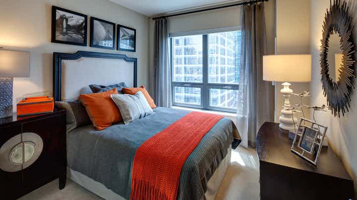 Bedroom at AMLI River North with queen bed with gray and orange bedspread and accent decor with window allowing for natural light