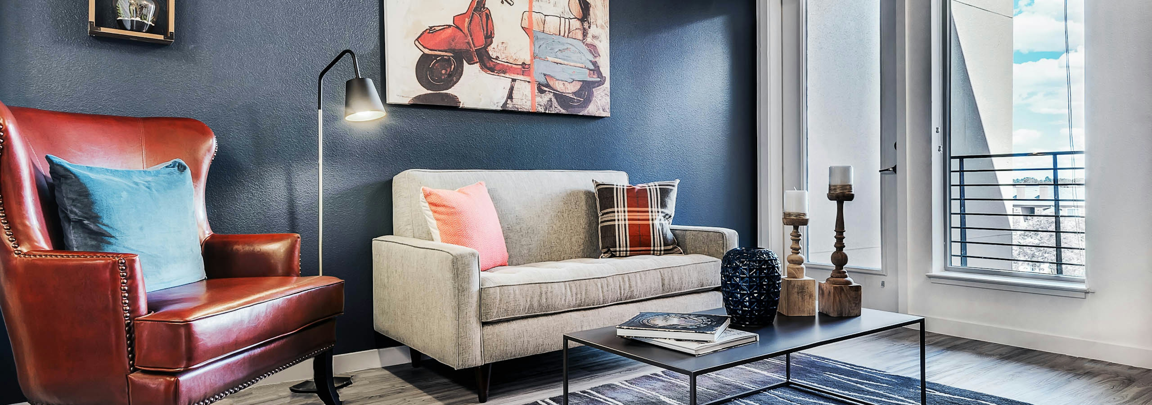 A living room at AMLI Cherry Creek apartments with a plush chair and couch with a coffee table and  artwork and window view