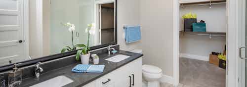 Double vanity bathroom at AMLI Decatur with dark countertops and white cabinets with a peak inside connecting walk in closet