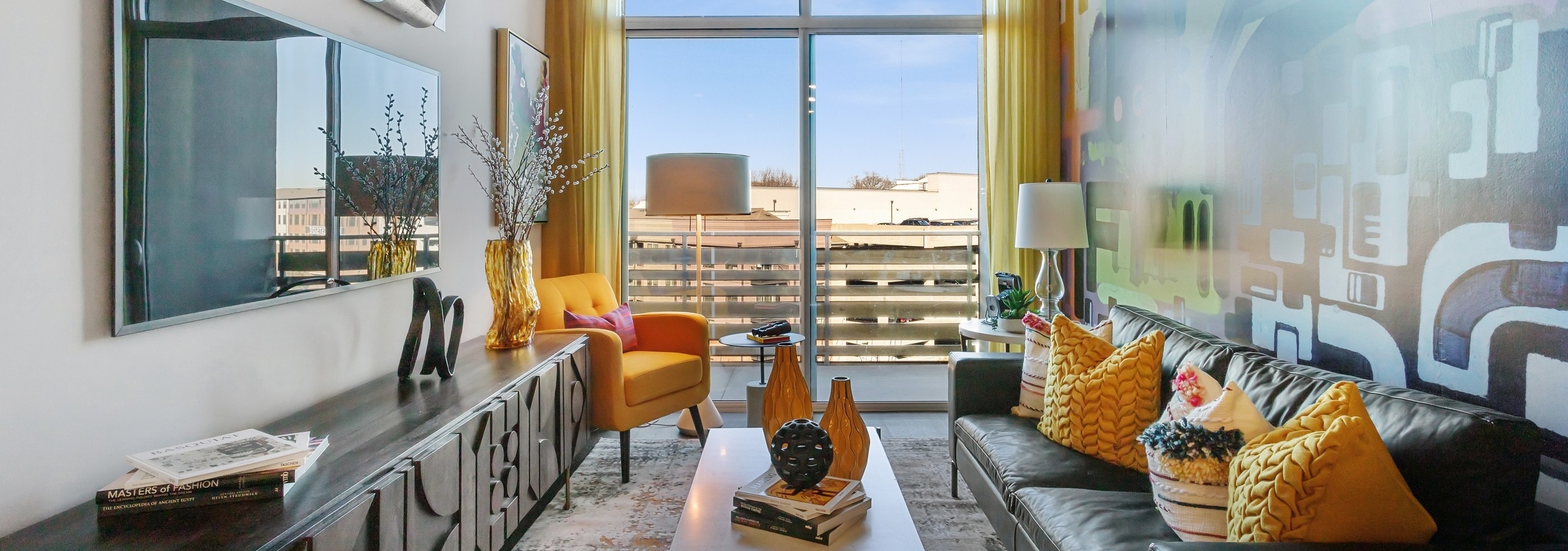Daytime view of colorful living room with leather couch and yellow accent pillows and large window at AMLI Westside apartments