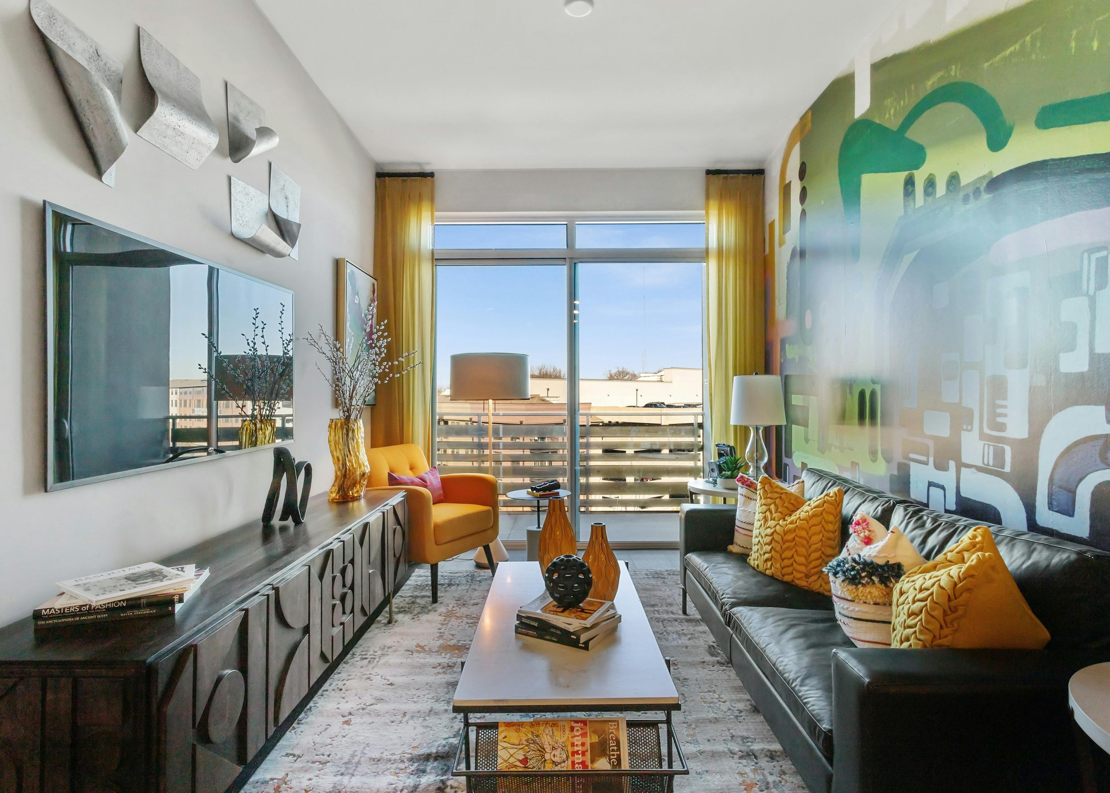 Daytime view of colorful living room with leather couch and yellow accent pillows and large window at AMLI Westside apartments