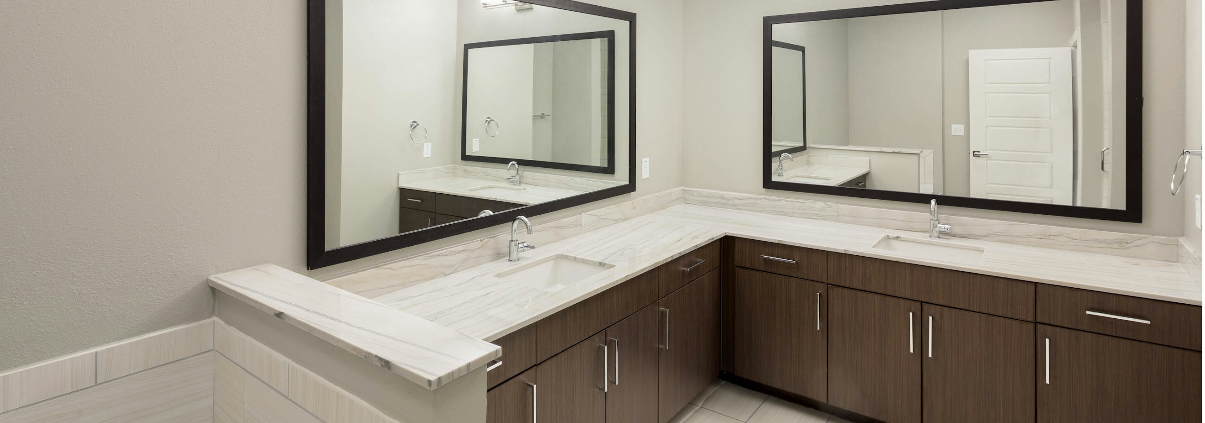 Spacious bathroom at AMLI on Aldrich with a framed mirror above each of the two vanity sinks featured and a white bathtub