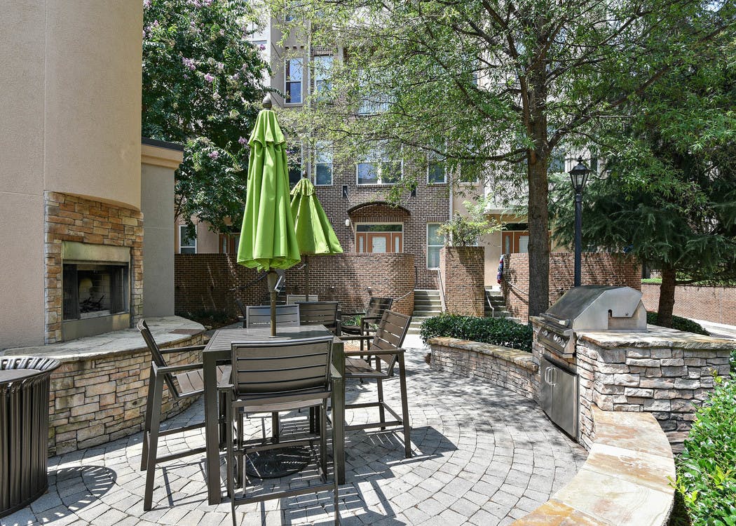 AMLI Lindbergh outdoor grilling area with fireplace and table and chairs with a green umbrella and stainless steel grill