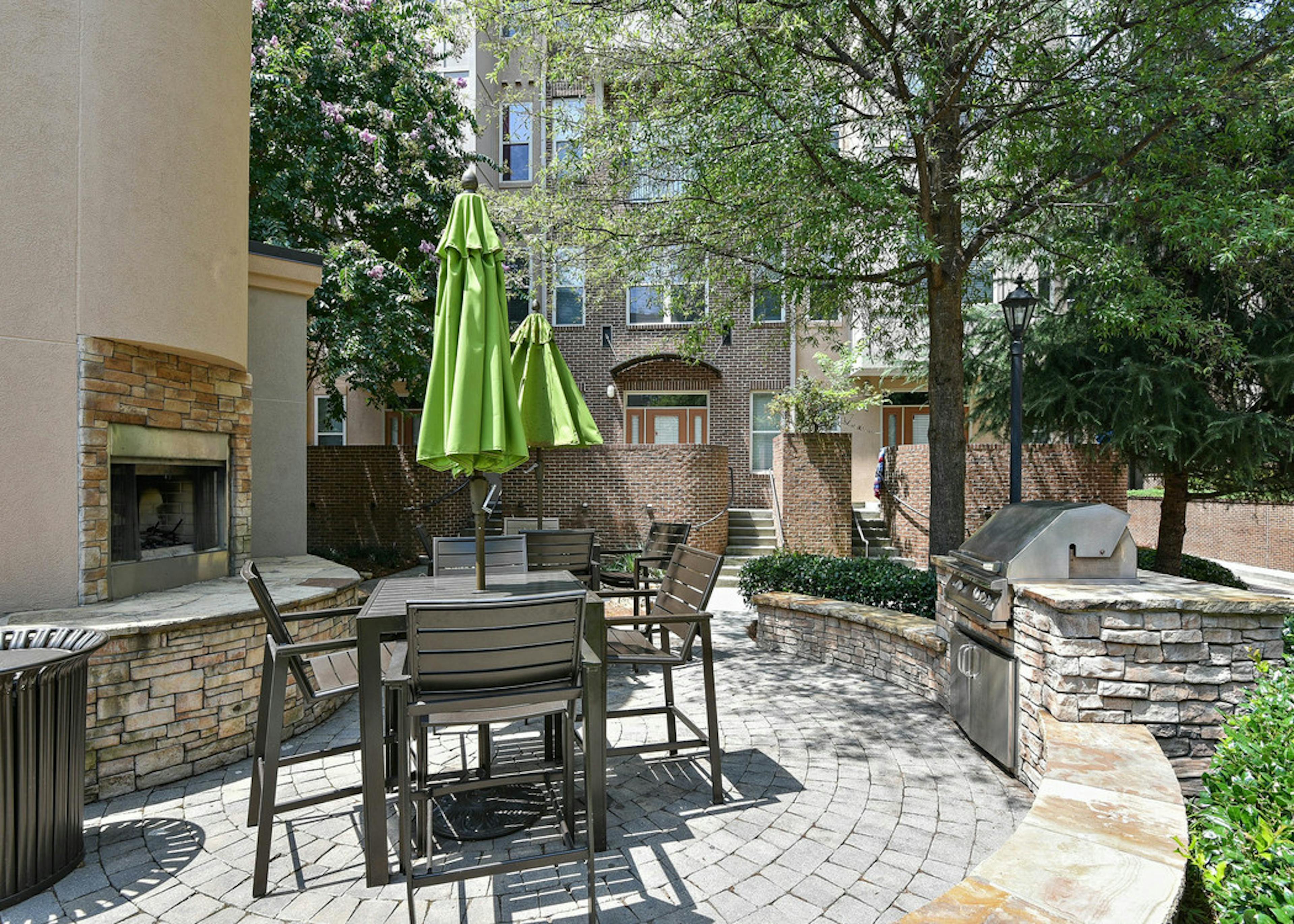AMLI Lindbergh outdoor grilling area with fireplace and table and chairs with a green umbrella and stainless steel grill