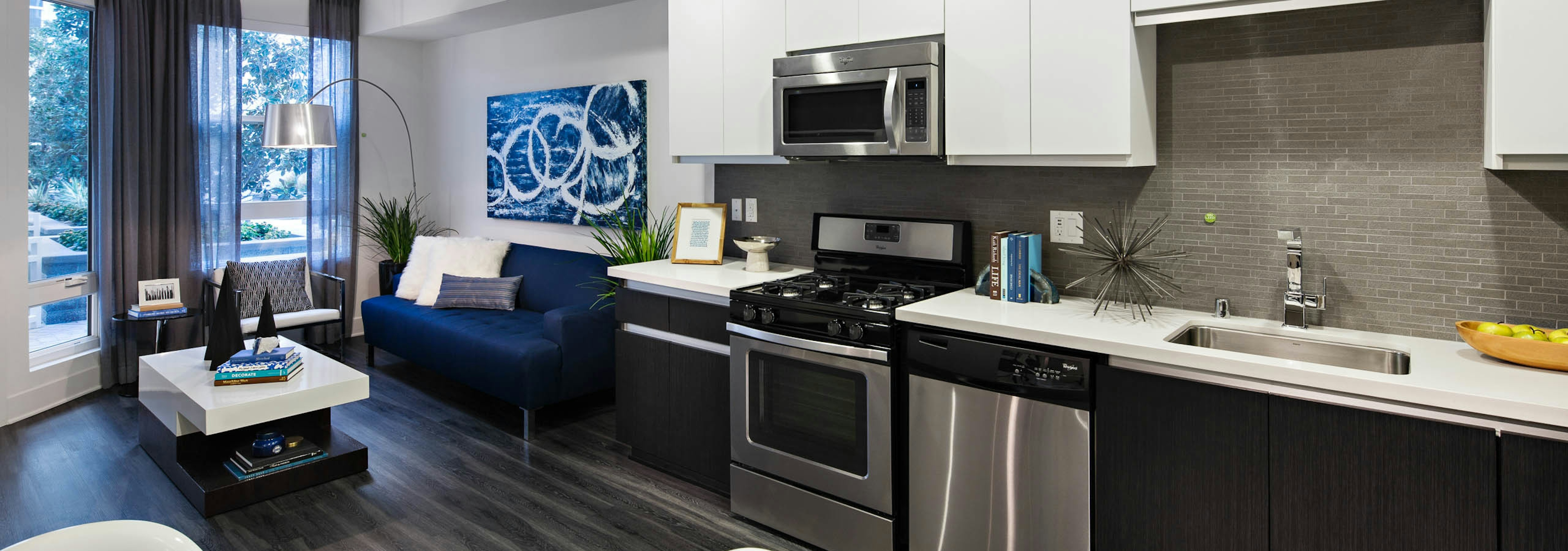 Interior of AMLI Lex on Orange apartment kitchen with white cabinetry and living room with blue couch and hard wood floors 