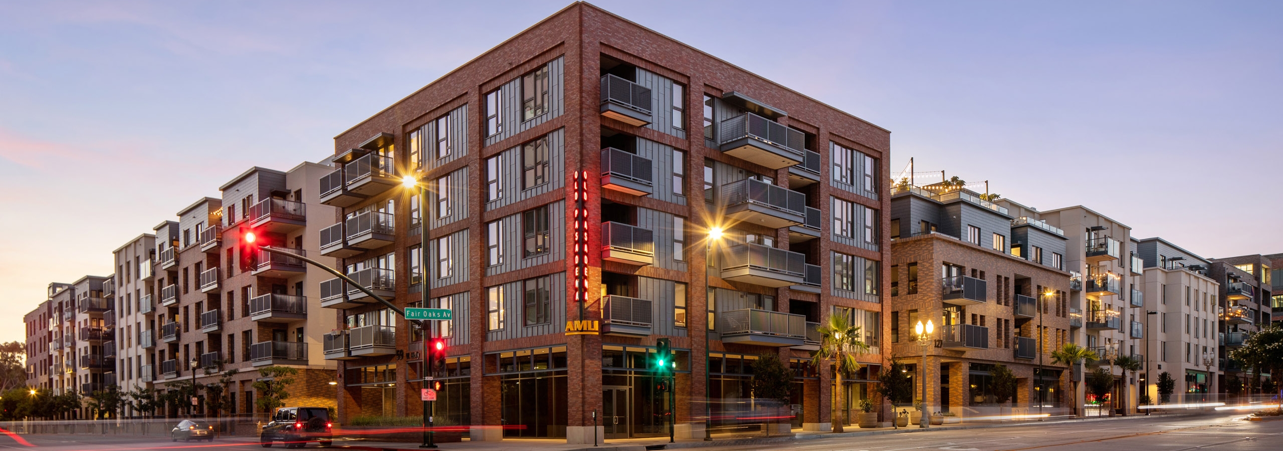 Corner view of AMLI Old Pasadena apartment building at dusk with brick façade and lit up monument signs and street lights