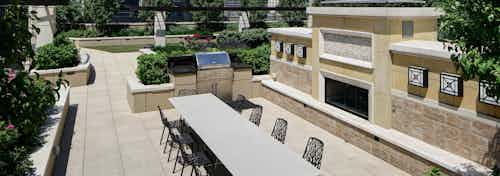 Exterior view of AMLI River North rooftop grill area with surrounding vibrant green plants and a long white table with chairs