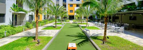 Outdoor courtyard area at AMLI 8800 with green grass, tropical landscape, bocce ball and corn hole games