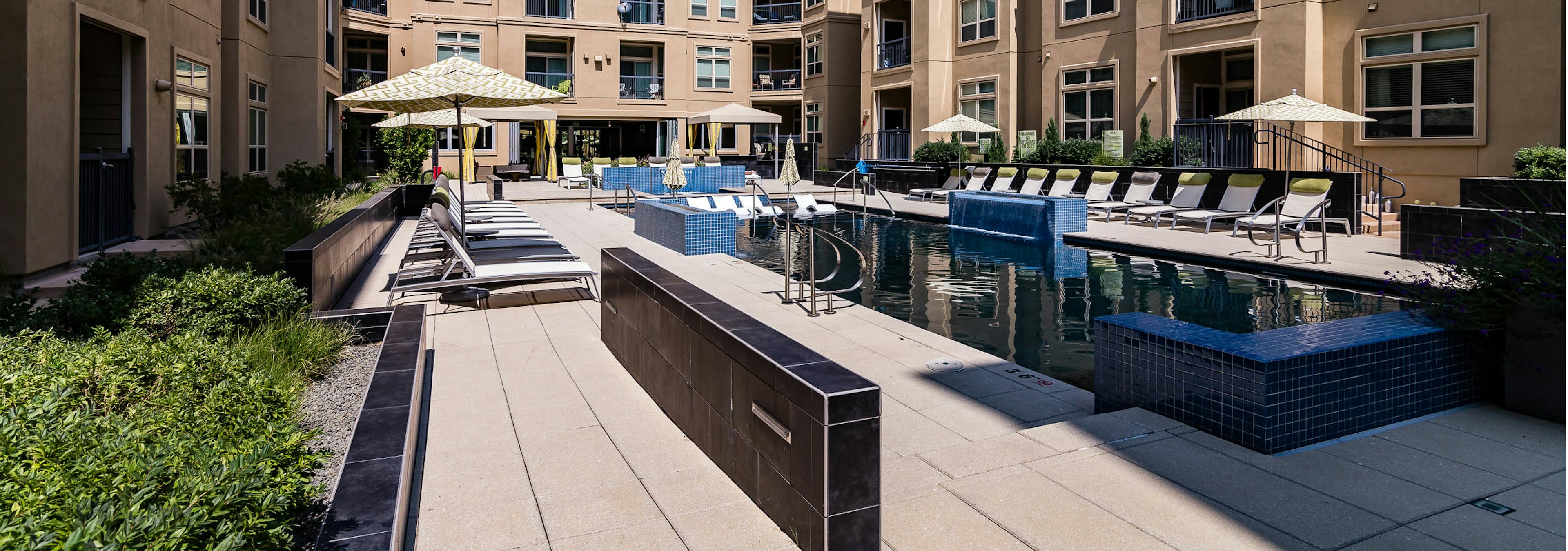 Daytime view of AMLI RidgeGate pool with blue tile surround and umbrellas over lounge chairs and two curtained cabanas