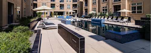 Daytime view of AMLI RidgeGate pool with blue tile surround and umbrellas over lounge chairs and two curtained cabanas