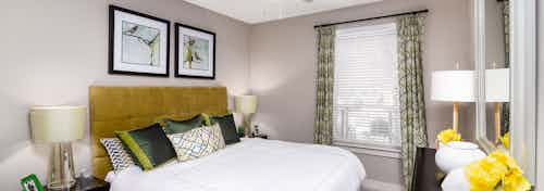 Interior view of a bedroom at AMLI Riverfront Park apartments with a large mirror and lamps and art and decorative pillows