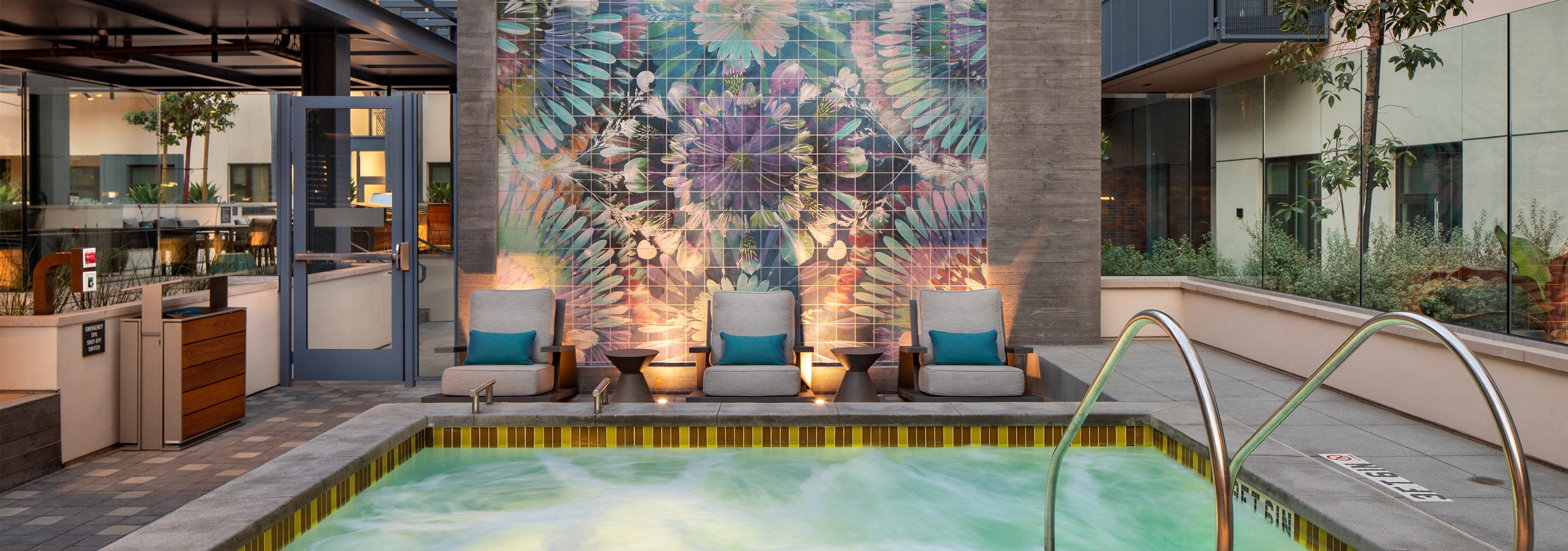Dusk view of AMLI Old Pasadena heated spa in front of a wall with a beautiful flower mural and three lounge chairs