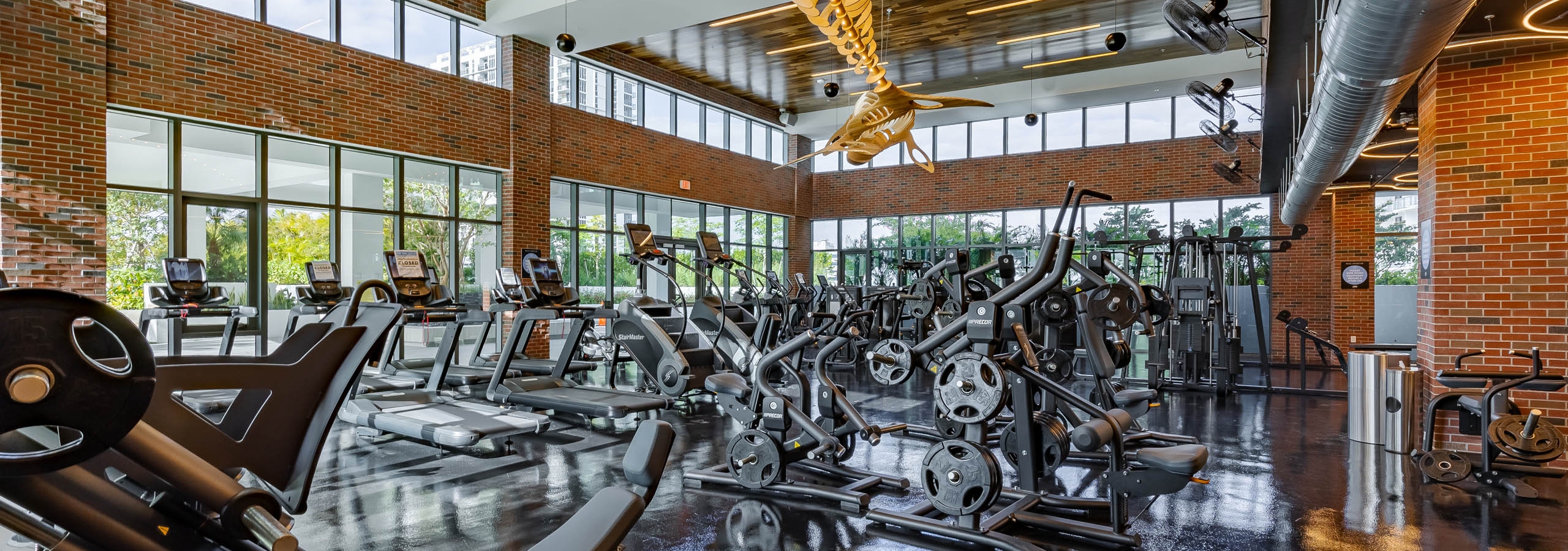 The fitness center at AMLI Midtown Miami with weight machines and cardio equipment with brick walls and wooden chandelier
