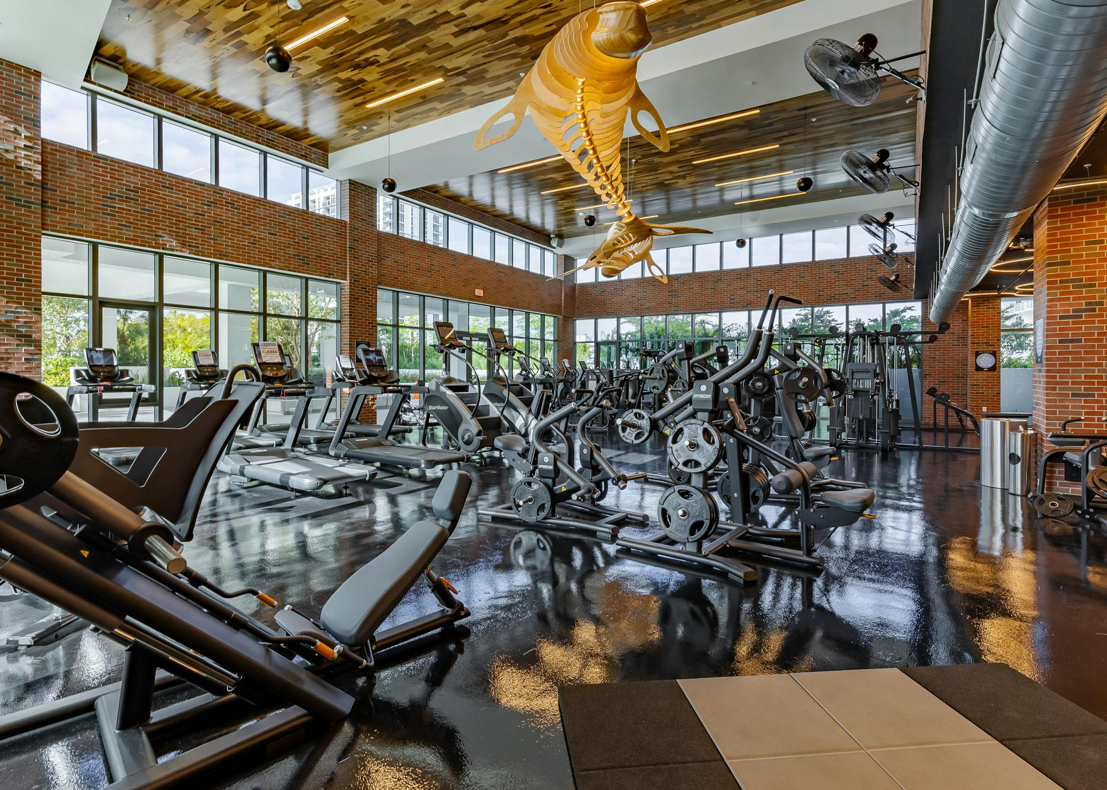 The fitness center at AMLI Midtown Miami with weight machines and cardio equipment with brick walls and wooden chandelier 