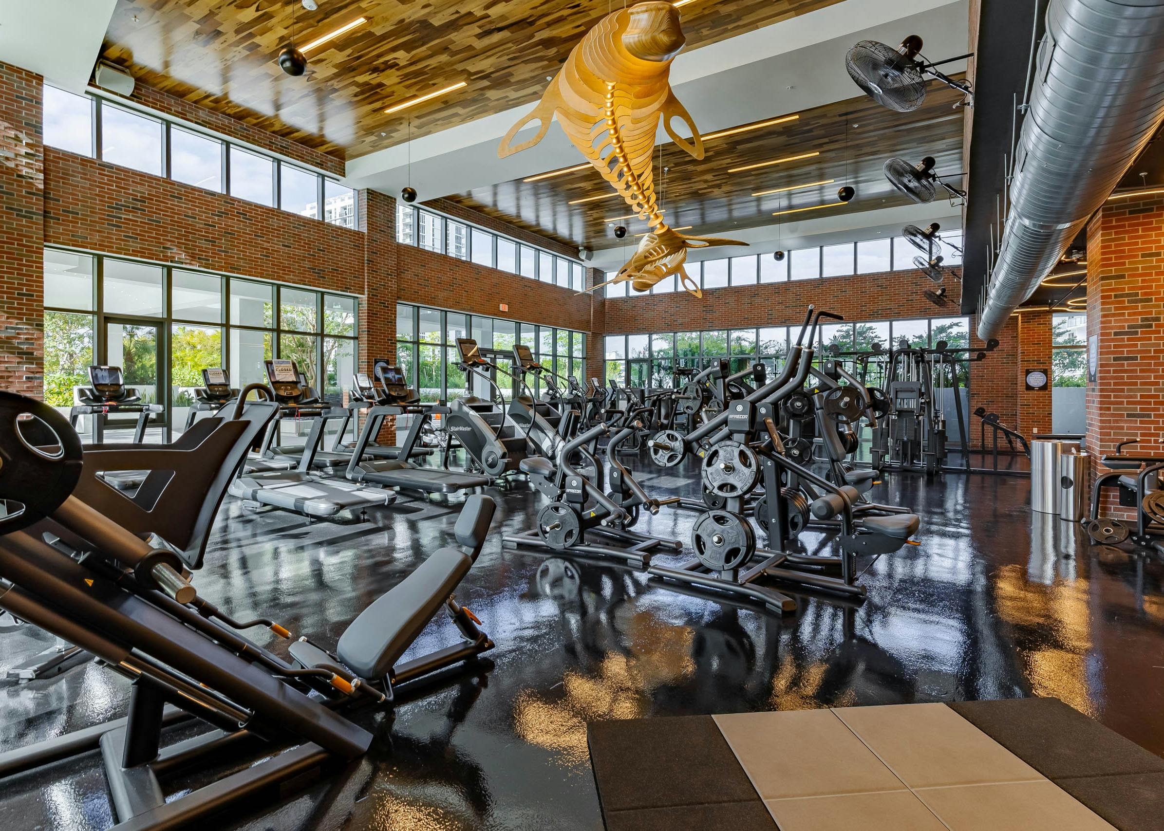 The fitness center at AMLI Midtown Miami with weight machines and cardio equipment with brick walls and wooden chandelier