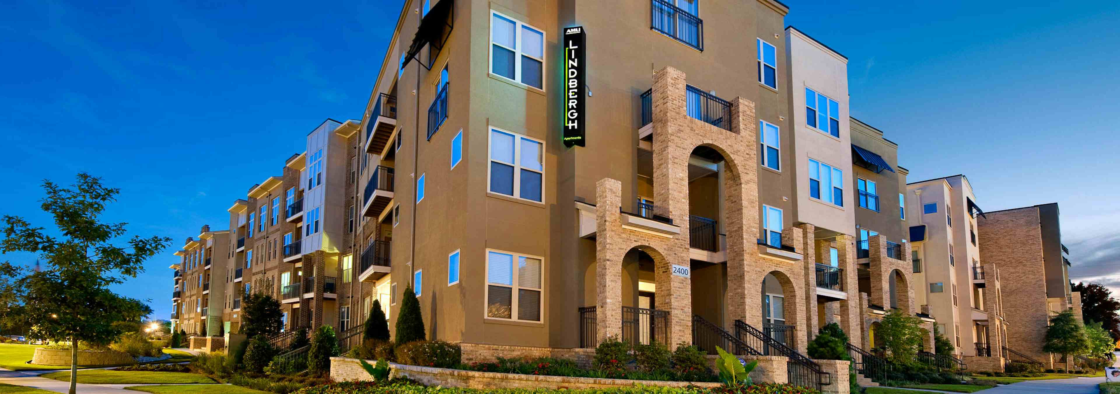 Exterior image of AMLI Lindbergh apartment community building stucco facade at sunset with pristine landscaping