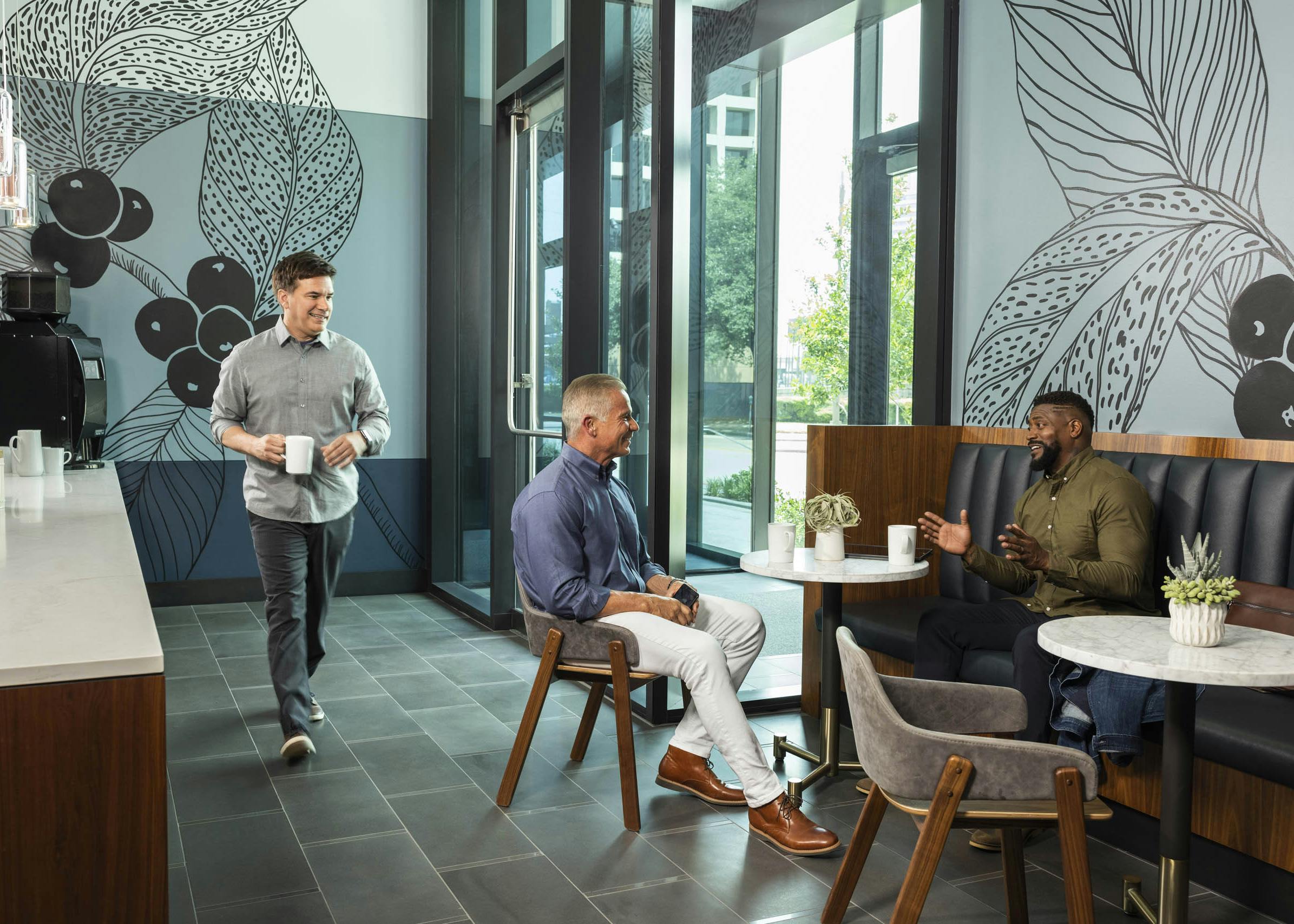Java café at AMLI Fountain Place with muraled walls and two men chatting over coffee while sitting in wooden leather chairs