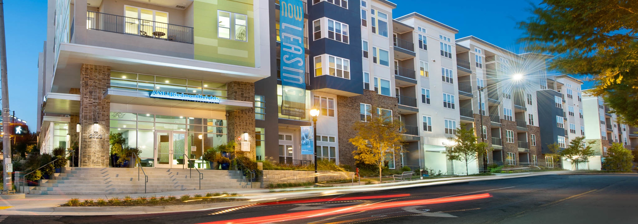 AMLI Piedmont Heights at night showing a well lit entrance with steps leading to front door with sign above and lush greenery