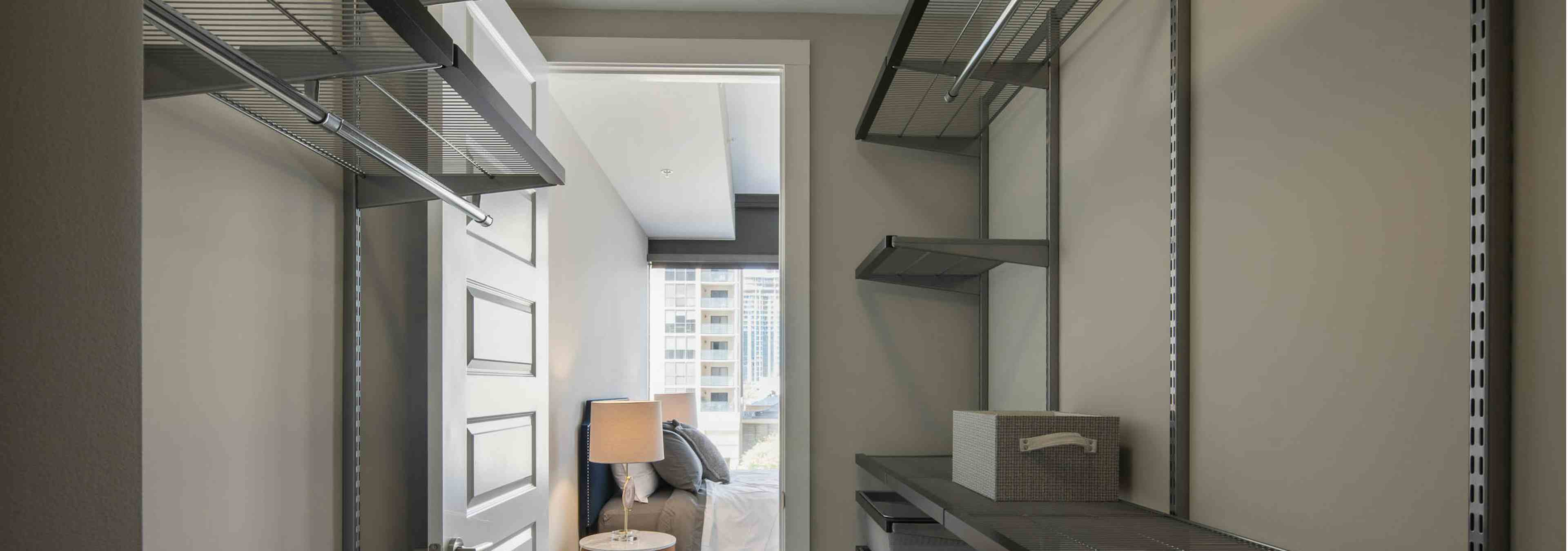 Interior of walk in closet at AMLI Arts Center with built in shelving and space to hang clothes with door opening to bedroom