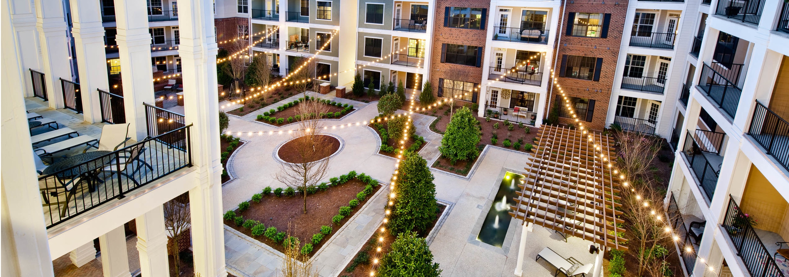 AMLI North Point courtyard with balconies and string lights above pavement for walking which is lined with pristine landscape