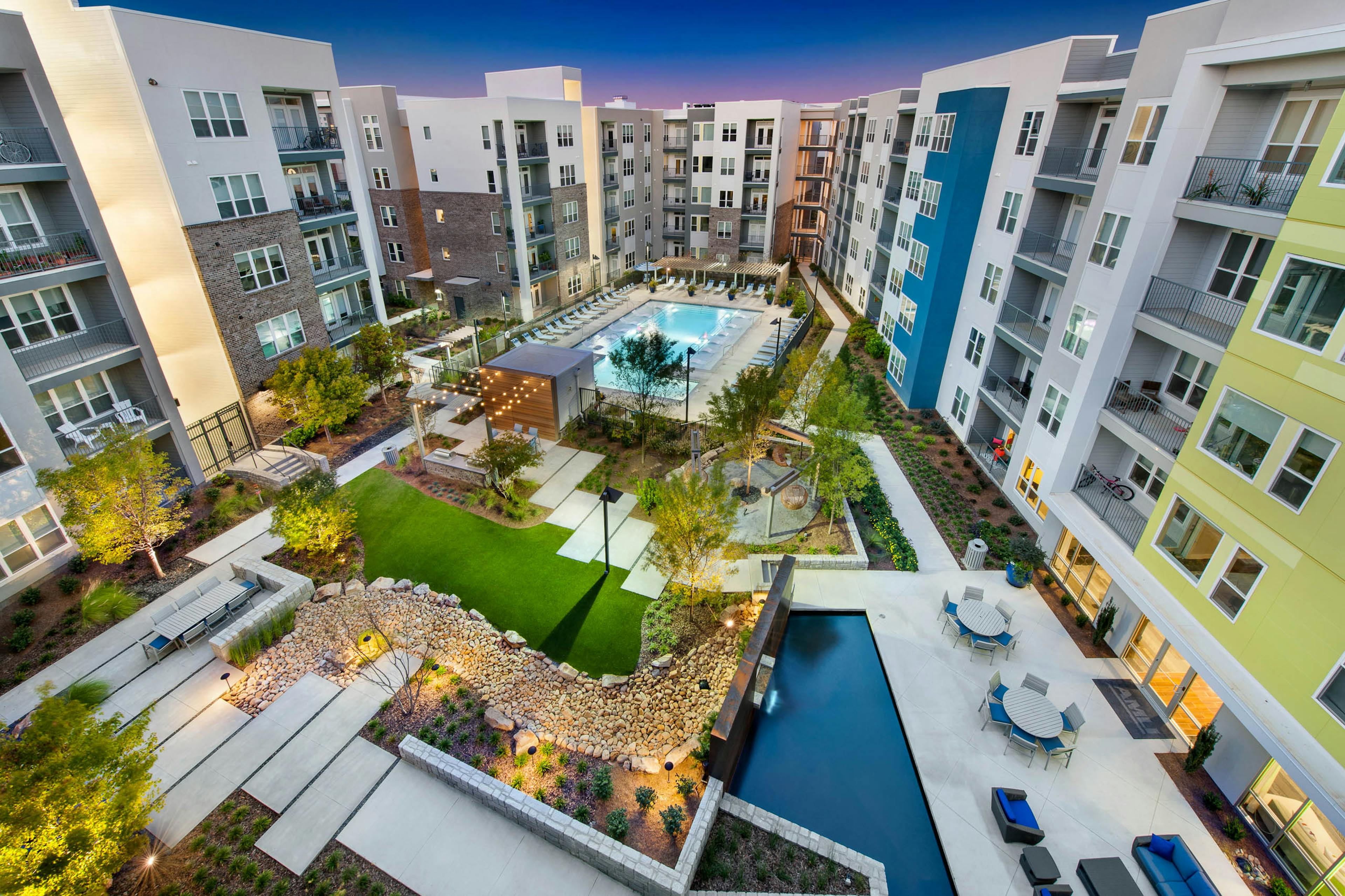 AMLI Piedmont Heights courtyard with large pool and lounge chairs surrounded by lit green areas and foliage at dusk