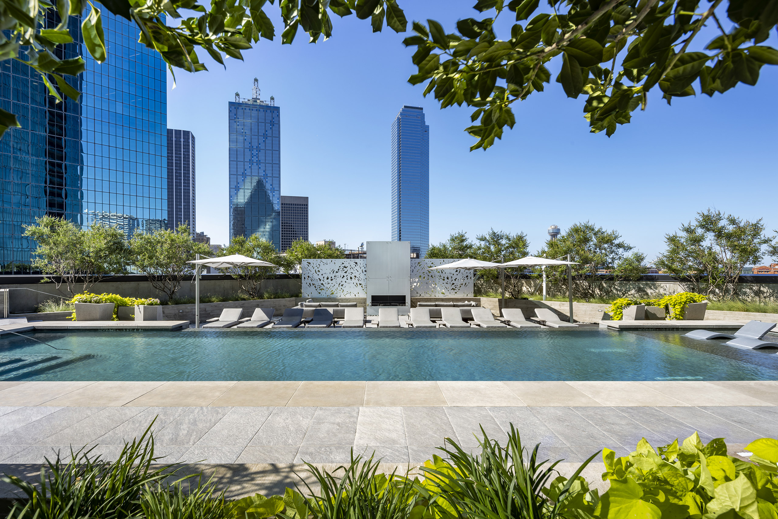 AMLI Fountain Place pool surrounded by grey stones deck with grey lounge chairs and fireplace in front of city skyline