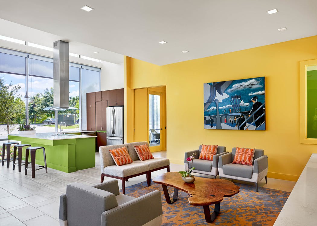 AMLI at Mueller clubroom with grey couches and chairs against a yellow wall with barstools at a green counter in background