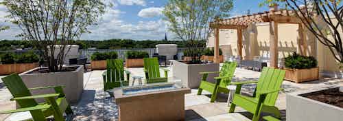 Rooftop deck at AMLI Evanston with grills and lime green lawn chairs next to large potted plants overlooking bright greenery