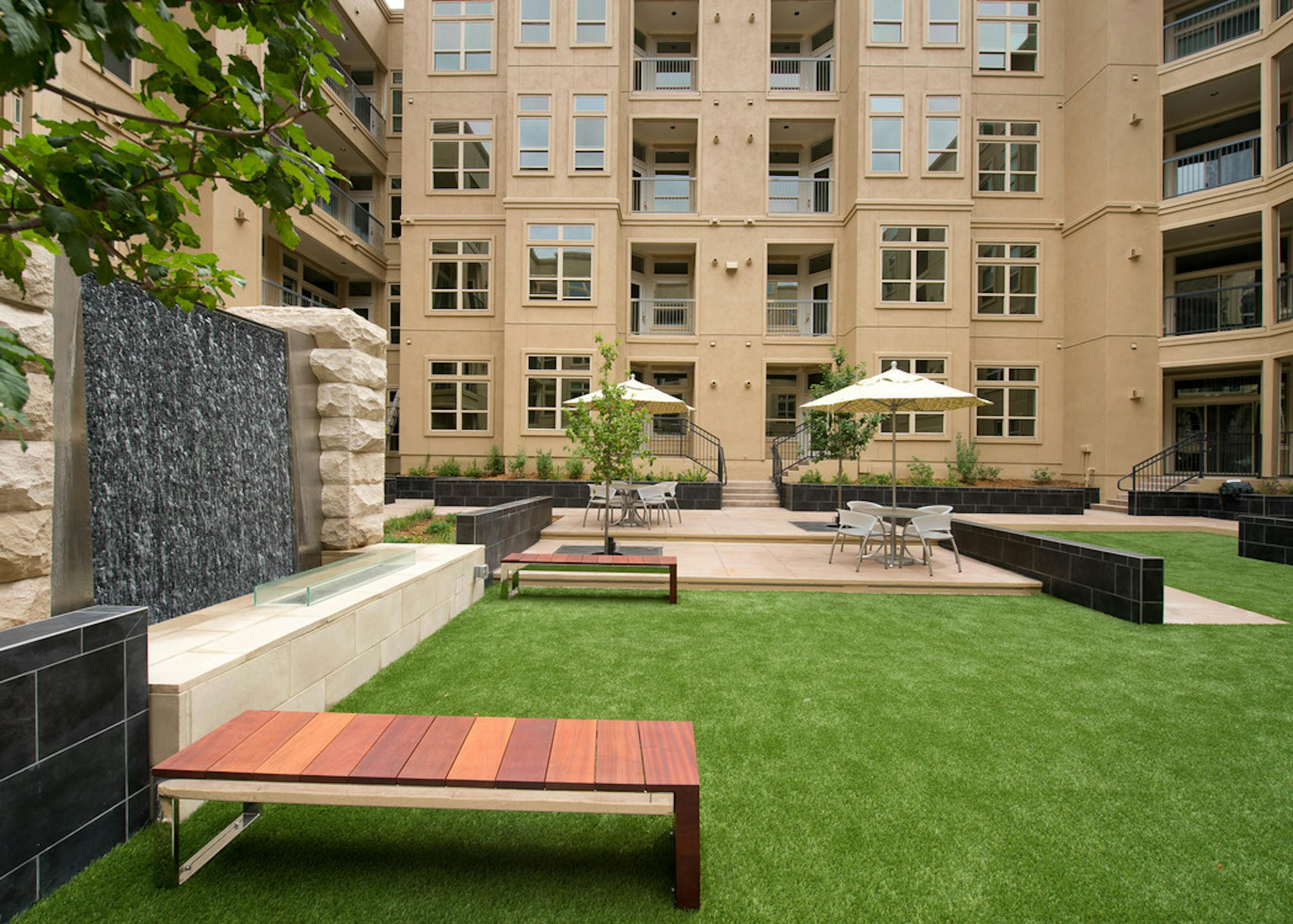 Daytime view of AMLI RidgeGate Zen garden with cascading stone waterfall, turf and various seating with umbrellas and trees