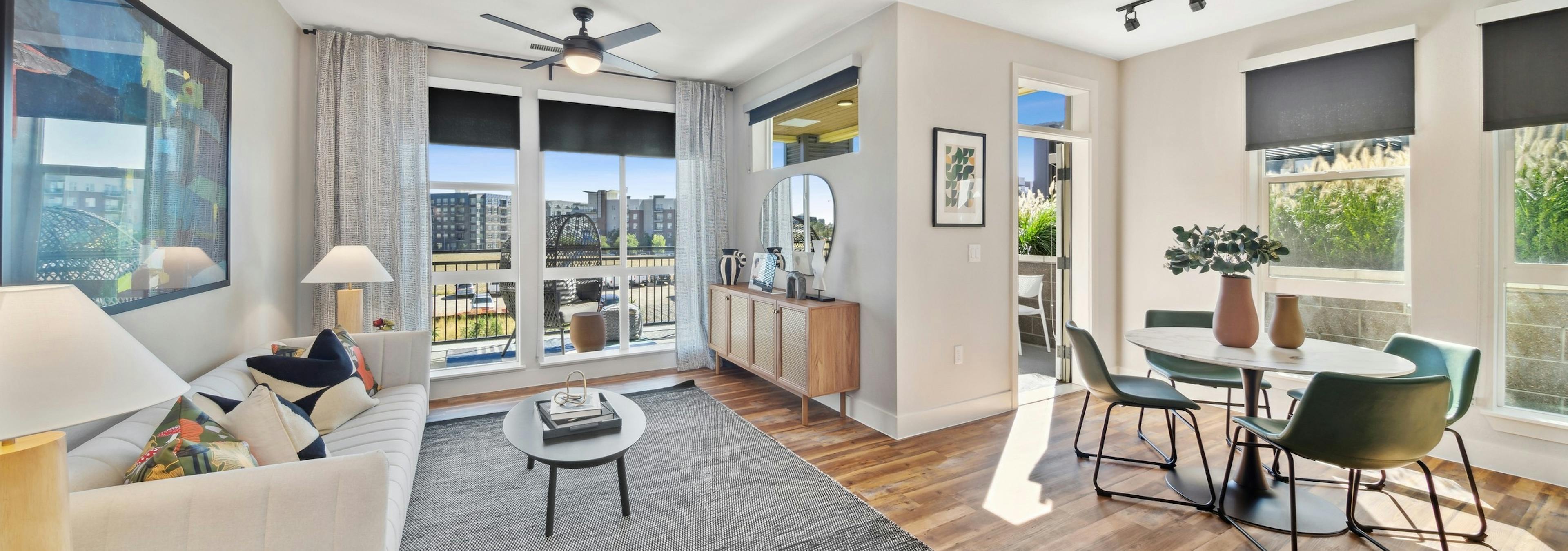 AMLI RiNo living room with white couch and grey rug  and dining table and chairs on wood floors with balcony with city view 