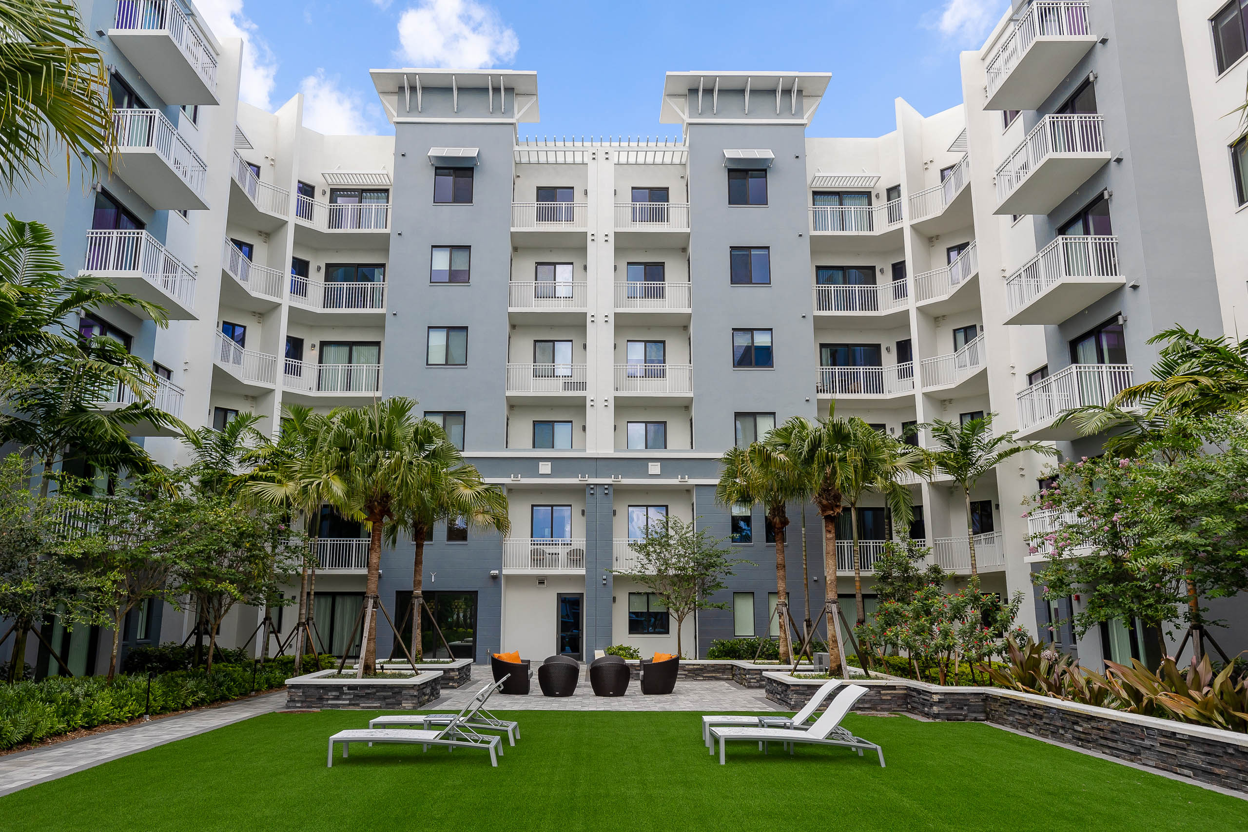 Daytime view of AMLI Park West courtyard with faux grass and white lounge chairs surrounded by lush tropical landscape