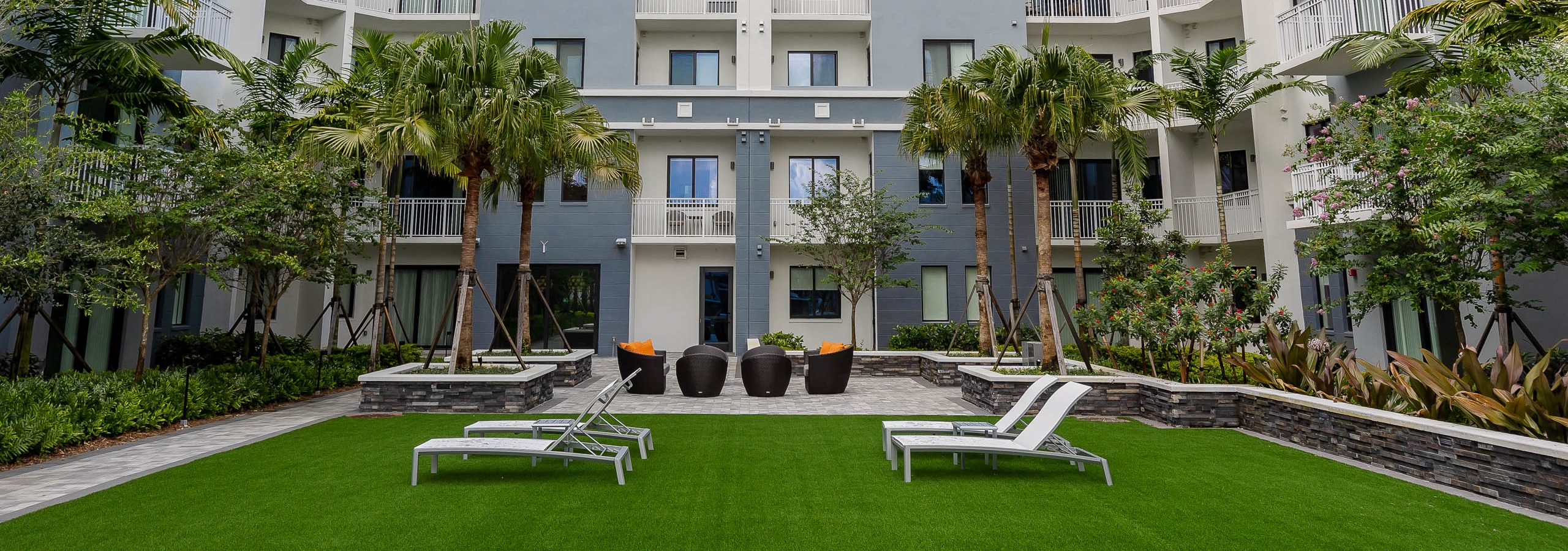 Daytime view of AMLI Park West courtyard with faux grass and white lounge chairs surrounded by lush tropical landscape