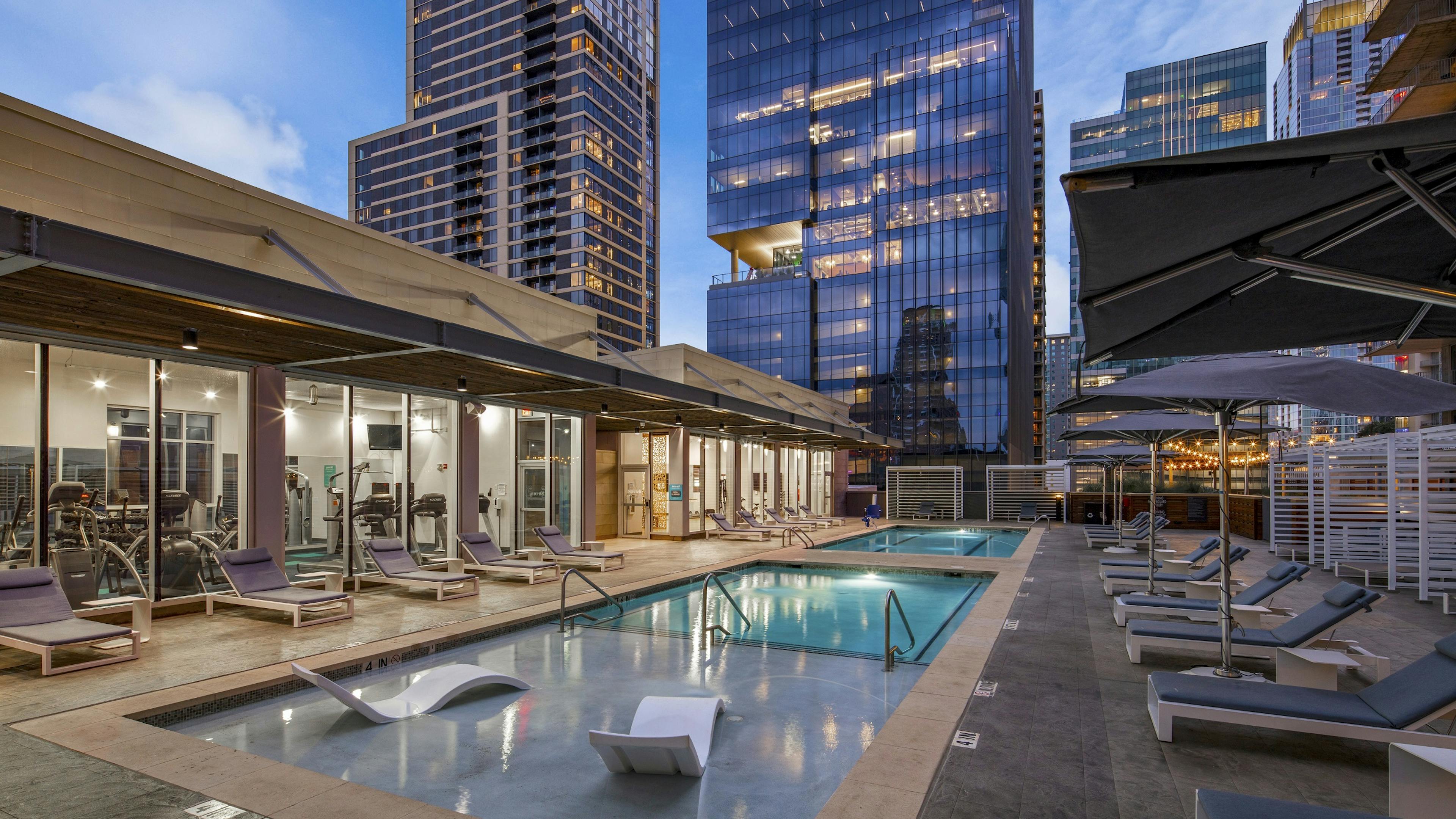 AMLI on 2ND skye deck pool surrounded by lounge seating and view into fitness center and overlooking neighboring skyscrapers