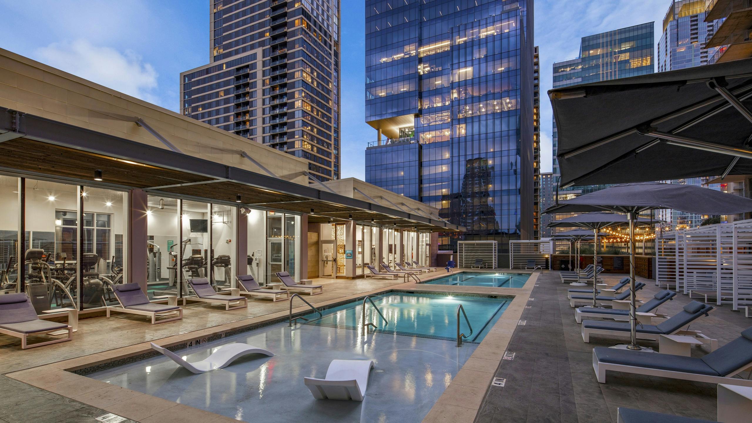 AMLI on 2ND skye deck pool surrounded by lounge seating and view into fitness center and overlooking neighboring skyscrapers