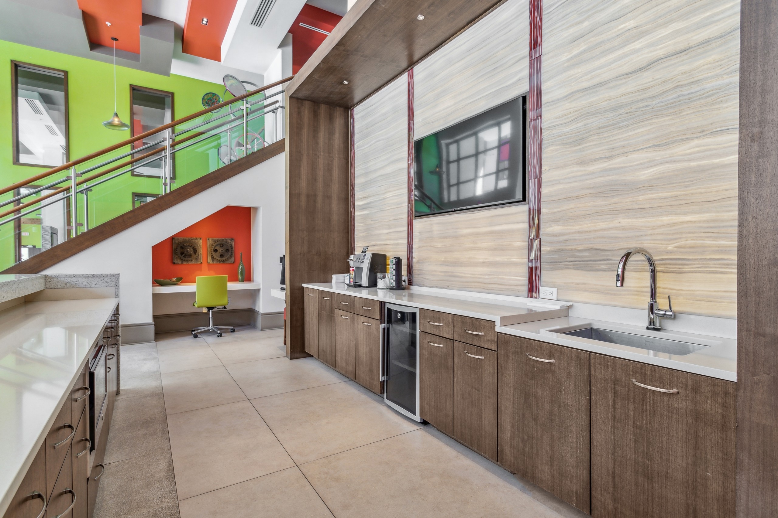 AMLI Ponce Park clubroom with serving kitchen and desk with orange wall set under staircase in front of bright green wall