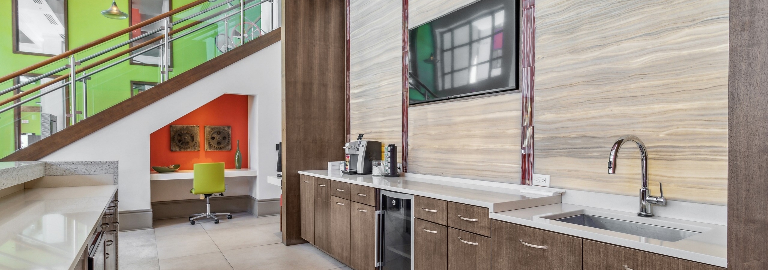 AMLI Ponce Park clubroom with serving kitchen and desk with orange wall set under staircase in front of bright green wall