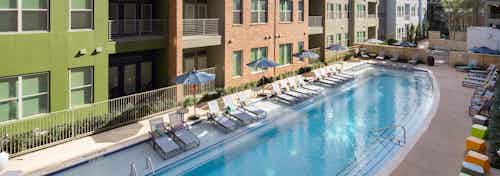 Exterior view of pool at AMLI at Mueller with blue umbrellas and white lounge chairs with facing building facade