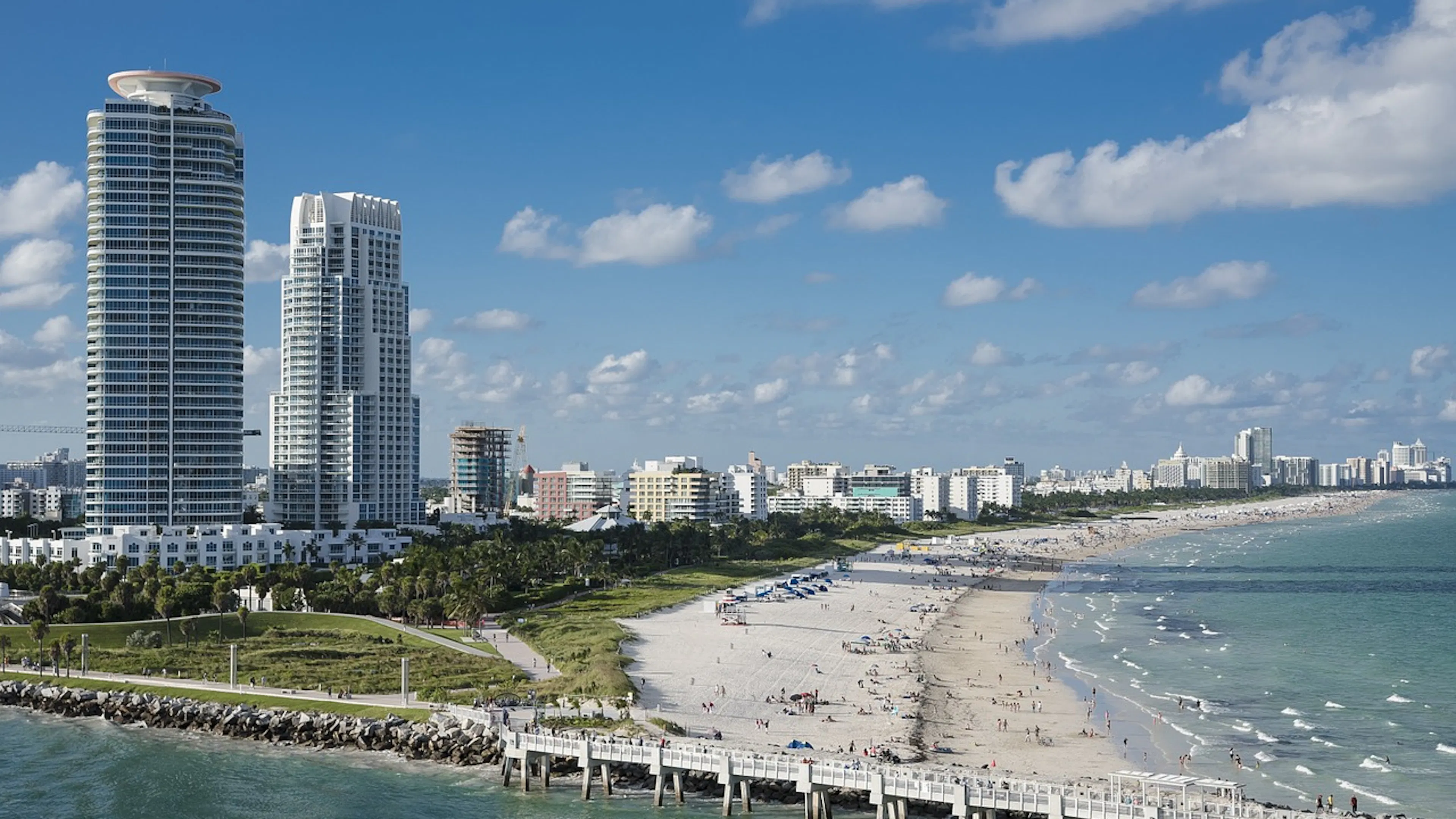 Miami beach scene with buildings along the shoreline and people enjoying the sandy beach and the weather under blue skies