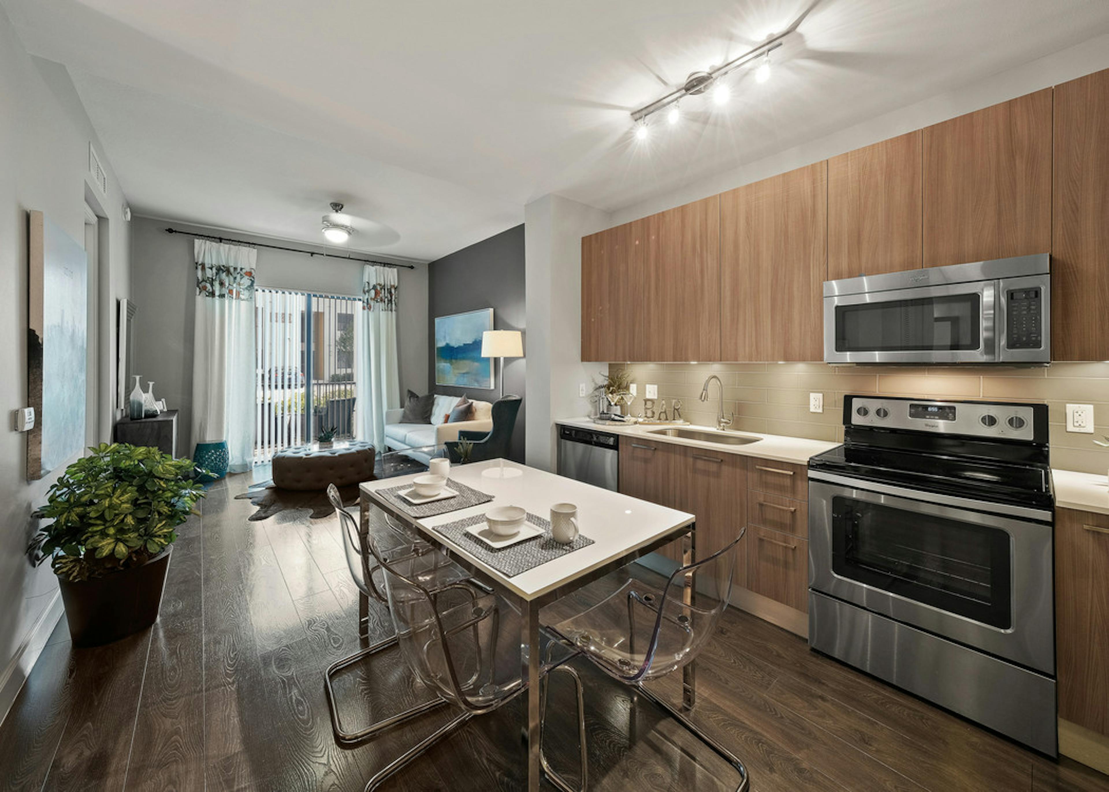 Interior view of AMLI 8800 apartment island kitchen with stainless steel appliances, granite counters and dark wood cabinetry