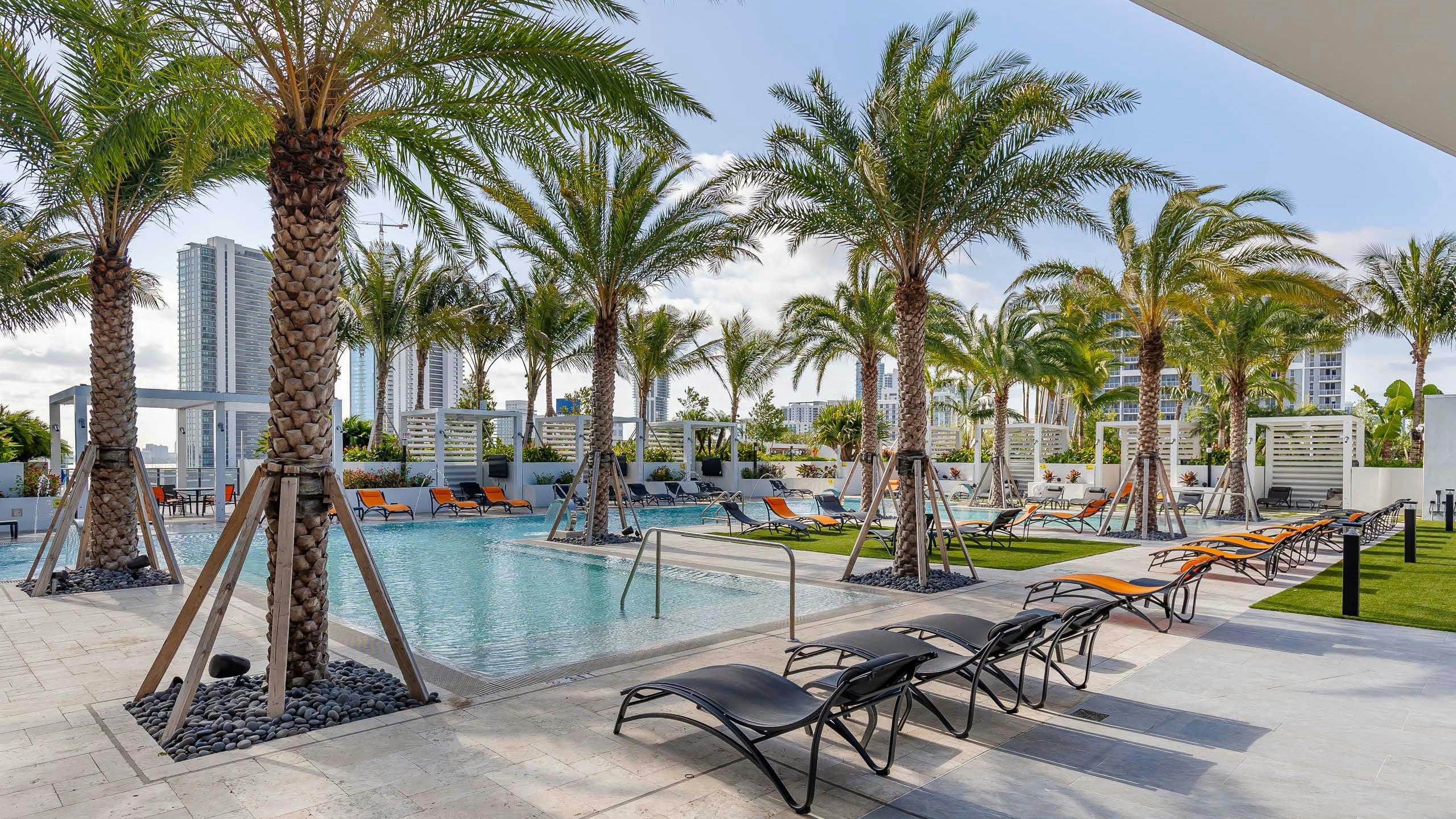 Daytime view of the AMLI Midtown Miami pool deck with orange and black lounge chairs and palm trees and a view of the city