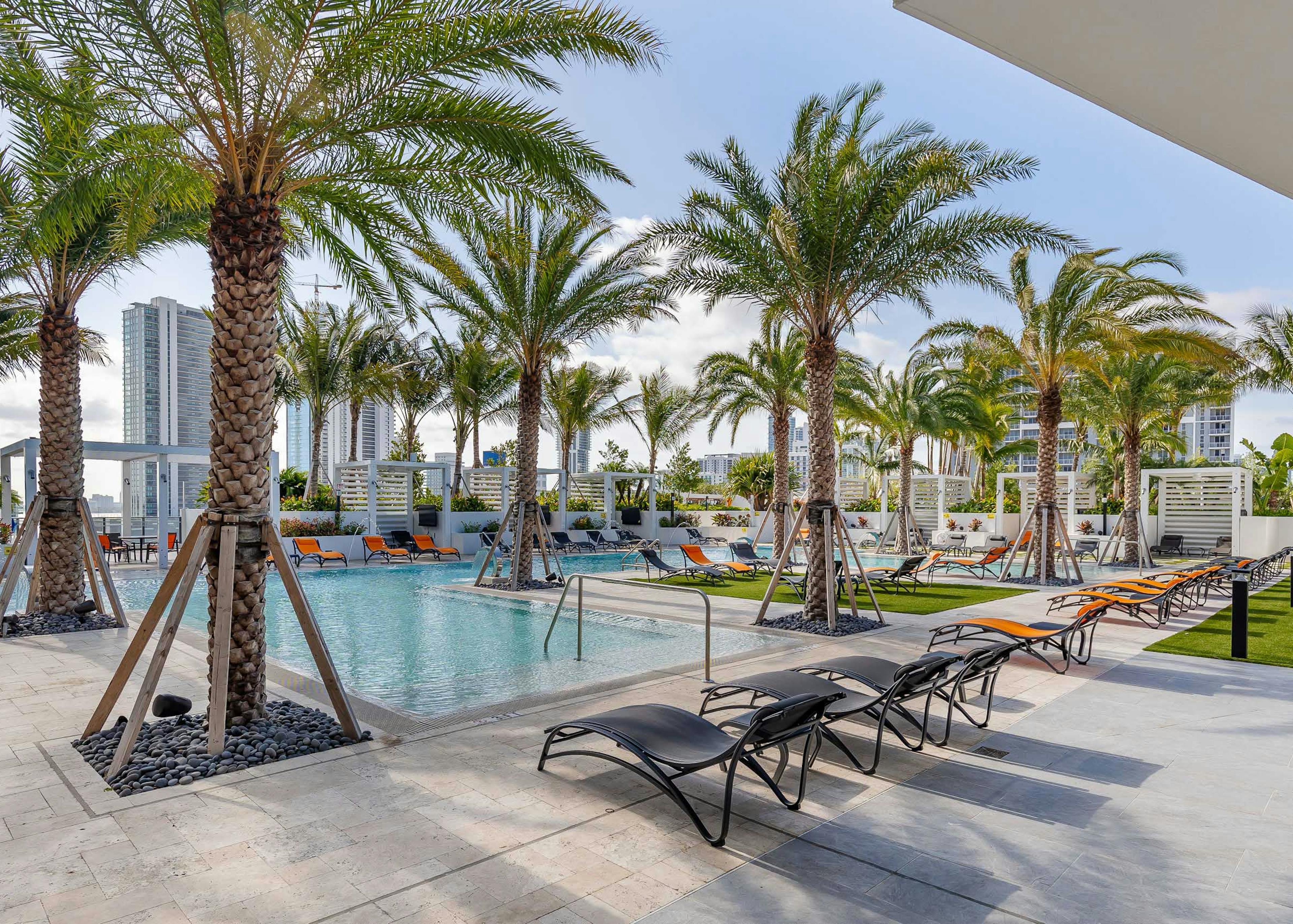 Daytime view of the AMLI Midtown Miami pool deck with orange and black lounge chairs and palm trees and a view of the city 
