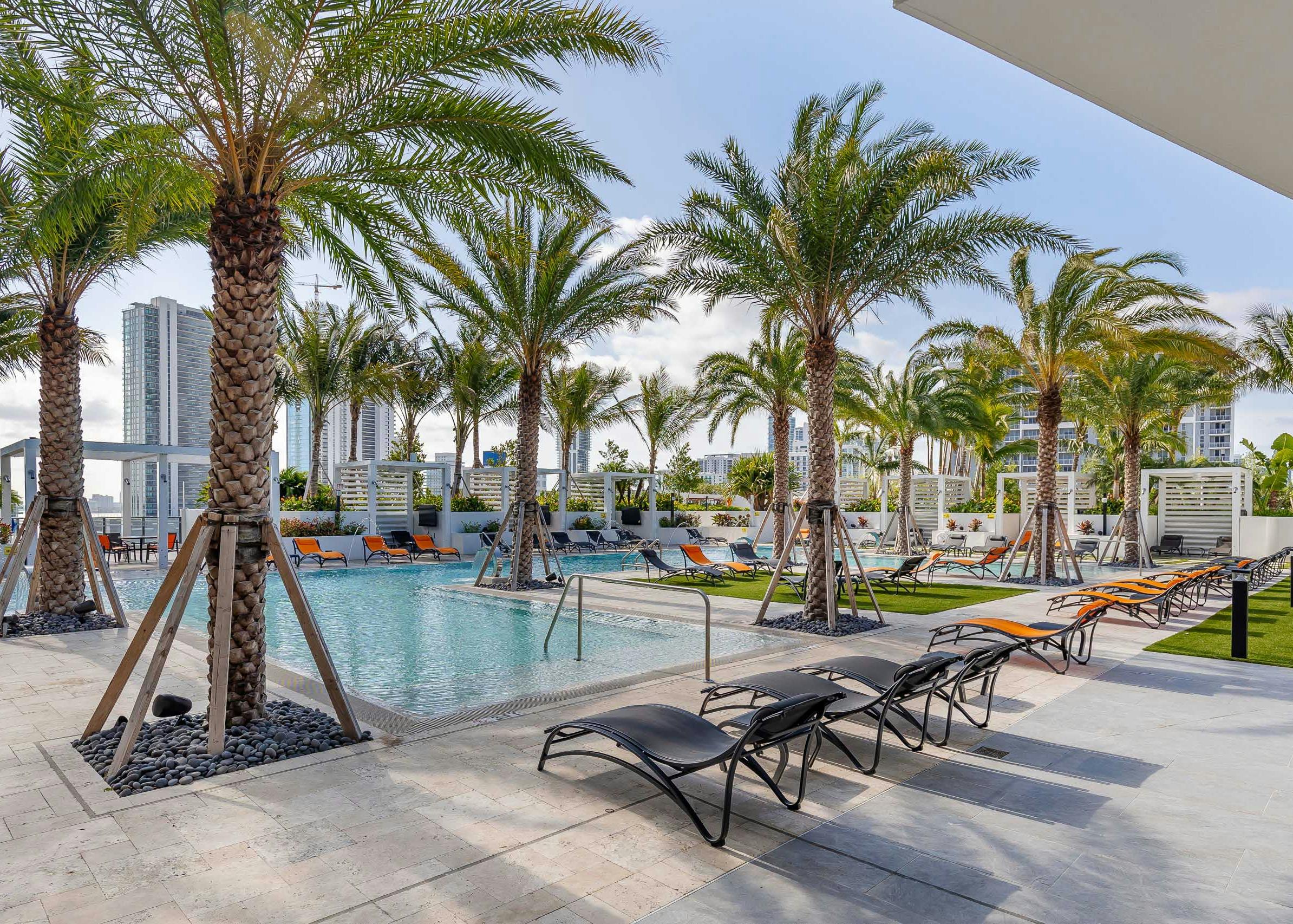 Daytime view of the AMLI Midtown Miami pool deck with orange and black lounge chairs and palm trees and a view of the city