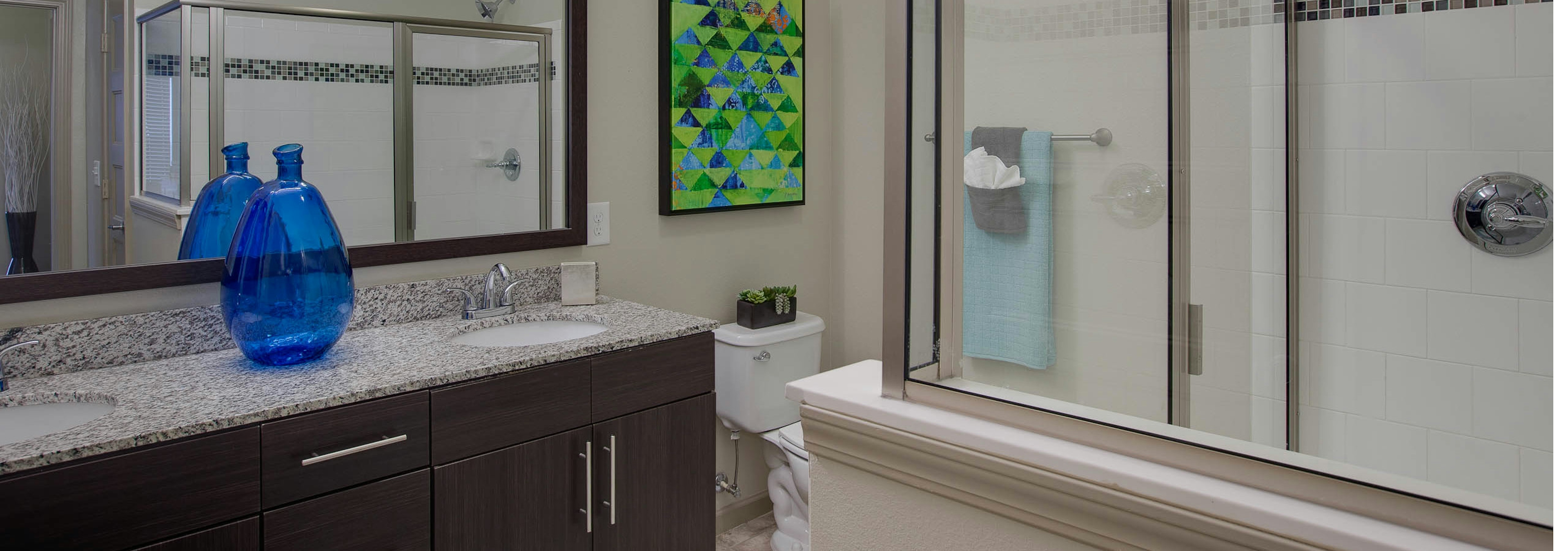 AMLI Ponce Park bathroom with double vanity with granite countertops with a toilet and a white shower tub with sliding doors