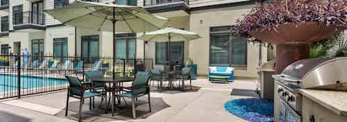 Outdoor grill area next to the pool at AMLI 5350 with table and chair sets with tan umbrellas and large stainless steel grill