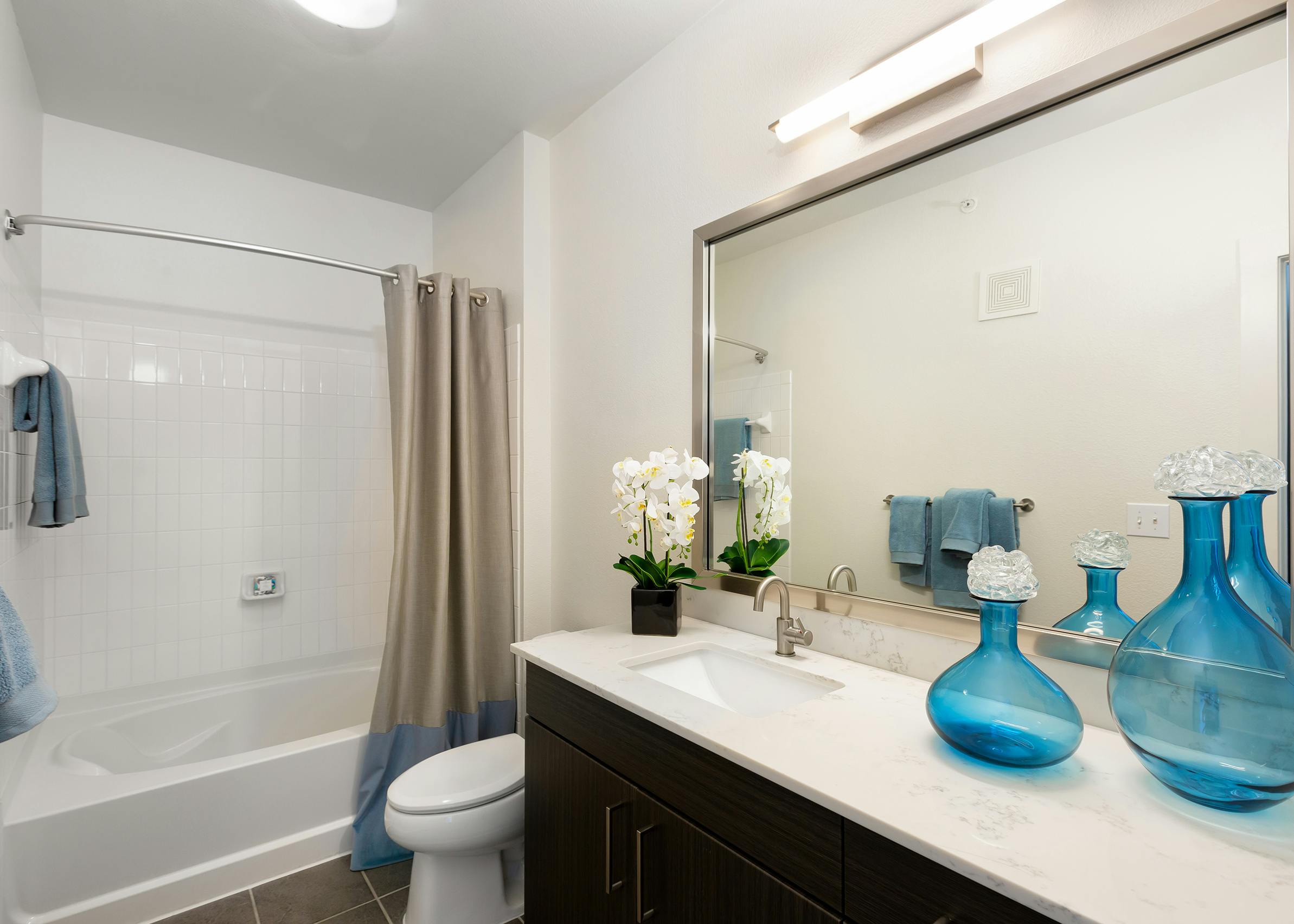 AMLI South Shore bathroom with dark wood single sink vanity with a quartz countertop and white shower tub with built in shelf