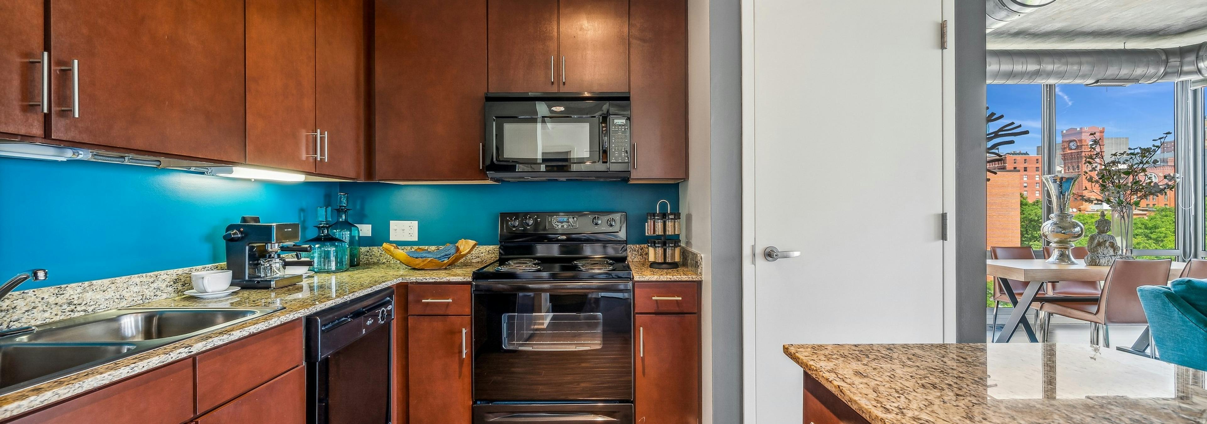 AMLI 900 apartment kitchen with medium brown wood cabinets and black appliances and blue backsplash and white closet door