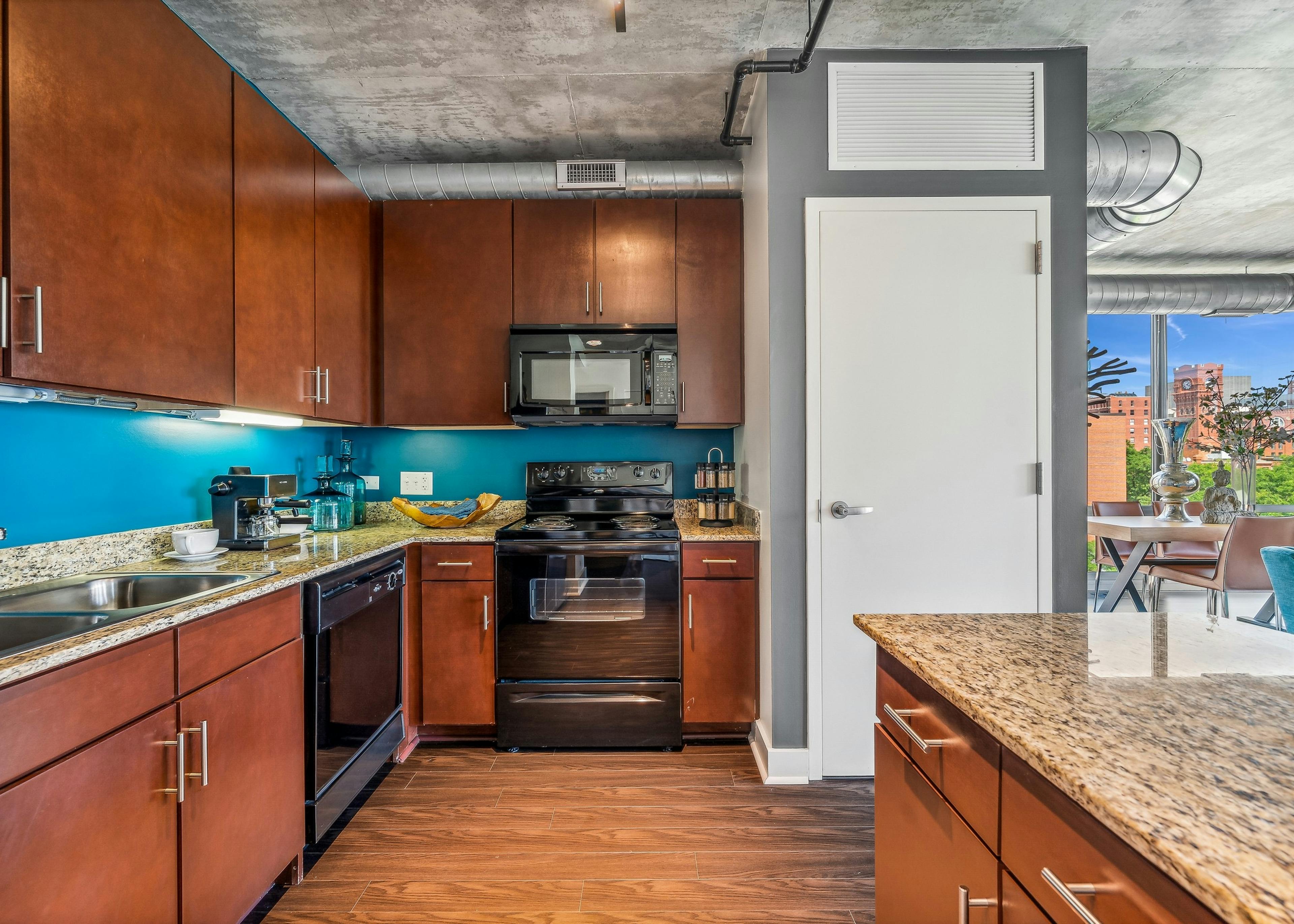 AMLI 900 apartment kitchen with medium brown wood cabinets and black appliances and blue backsplash and white closet door