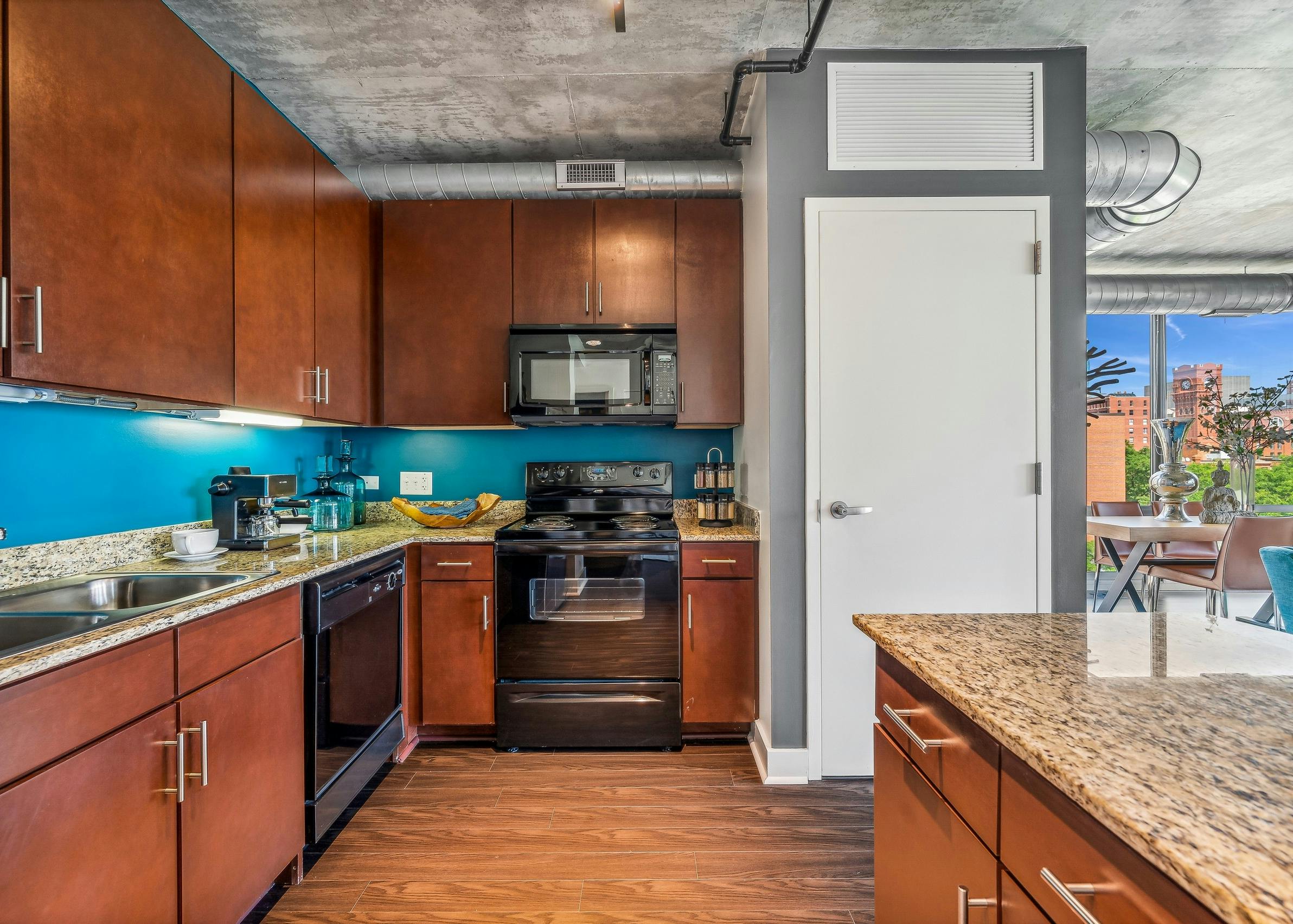 AMLI 900 apartment kitchen with medium brown wood cabinets and black appliances and blue backsplash and white closet door