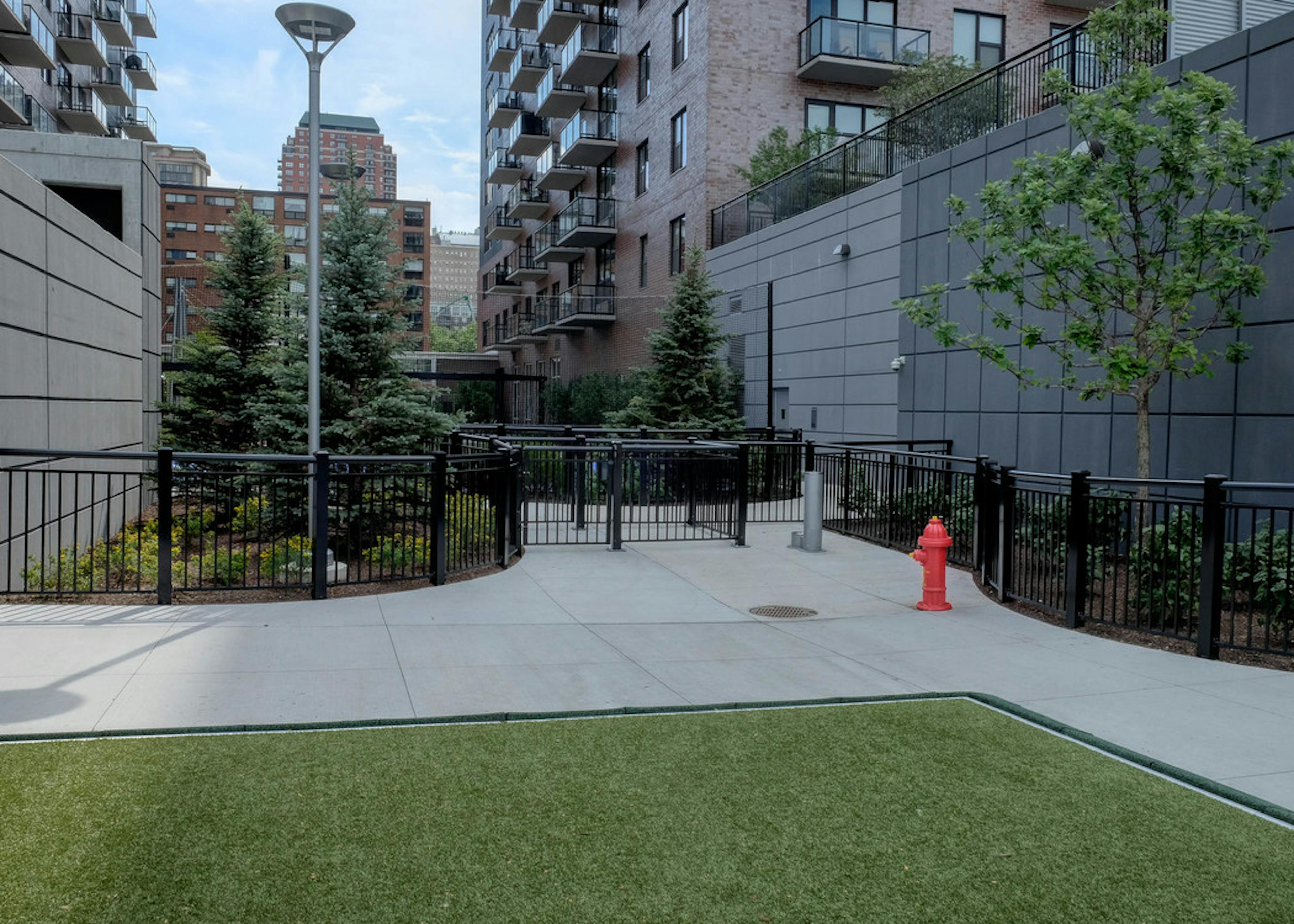 Exterior view of the gated dog run with artificial turf at the AMLI Lofts apartment community in the bright day time